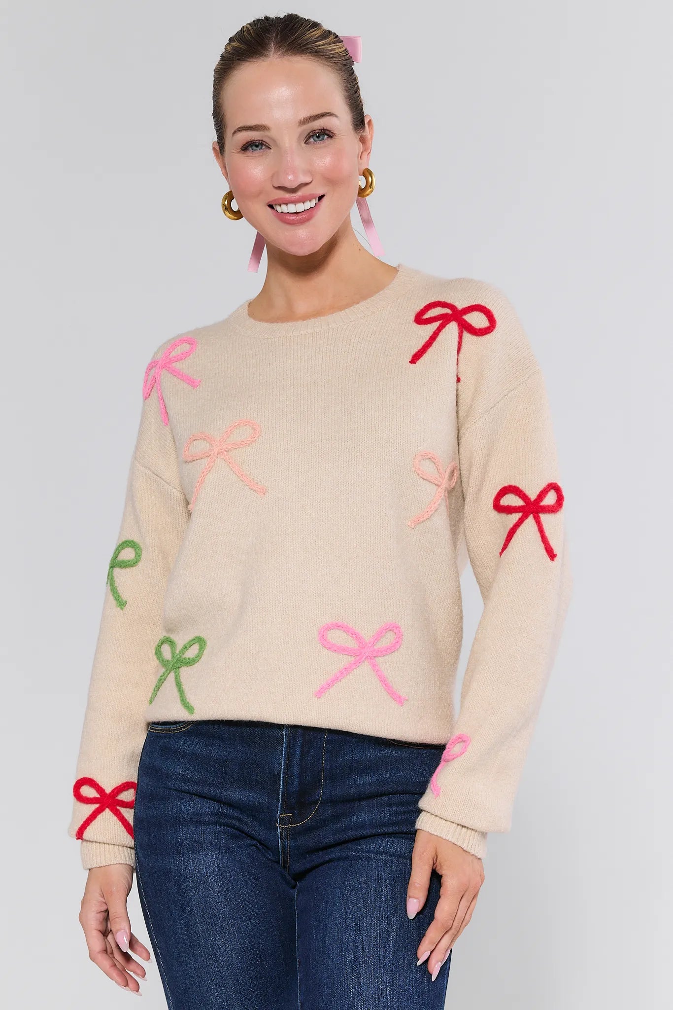 Woman wearing a beige Giselle Sweater with colorful bows on a plain background