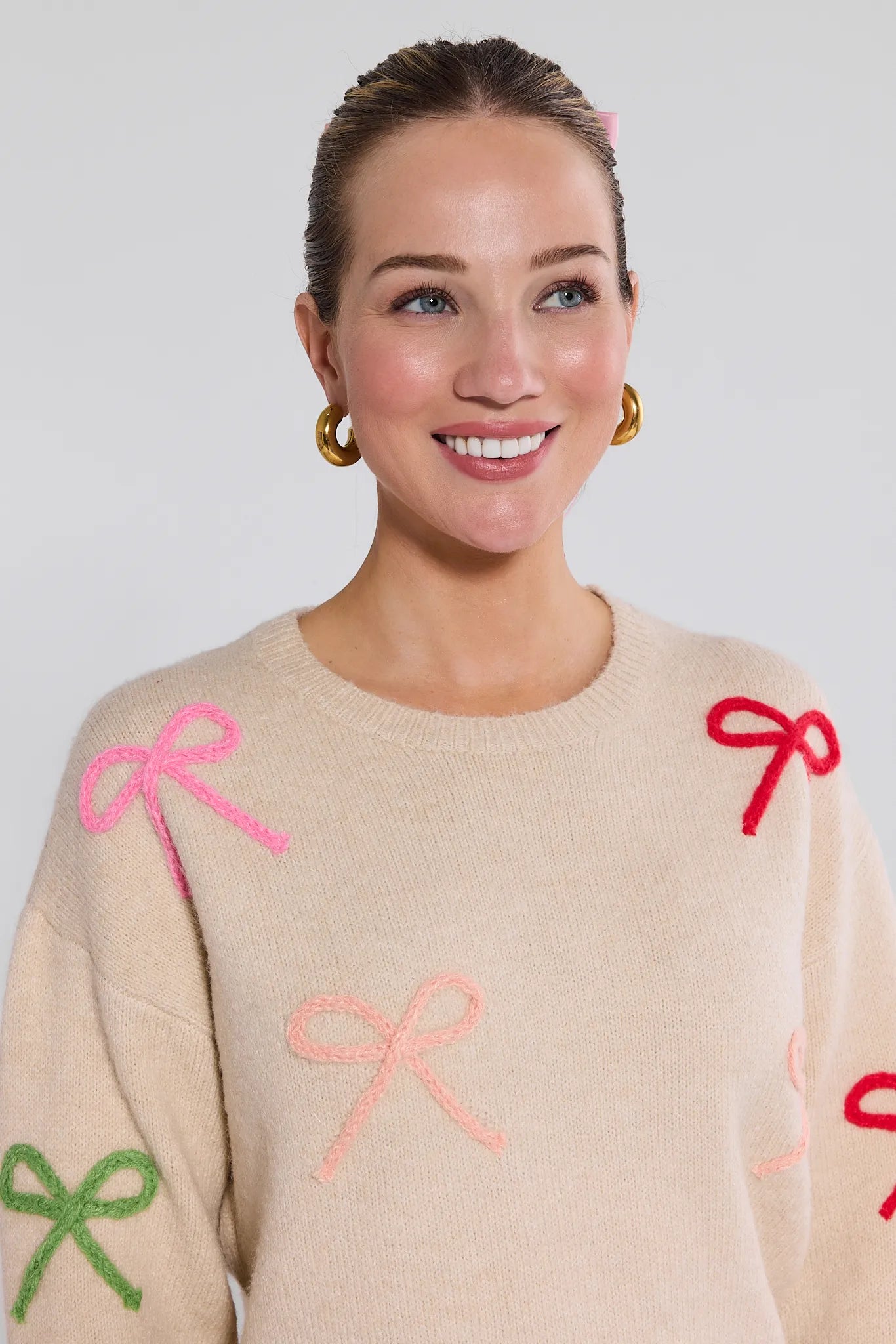Woman wearing a beige Giselle Sweater with colorful bows on a plain background