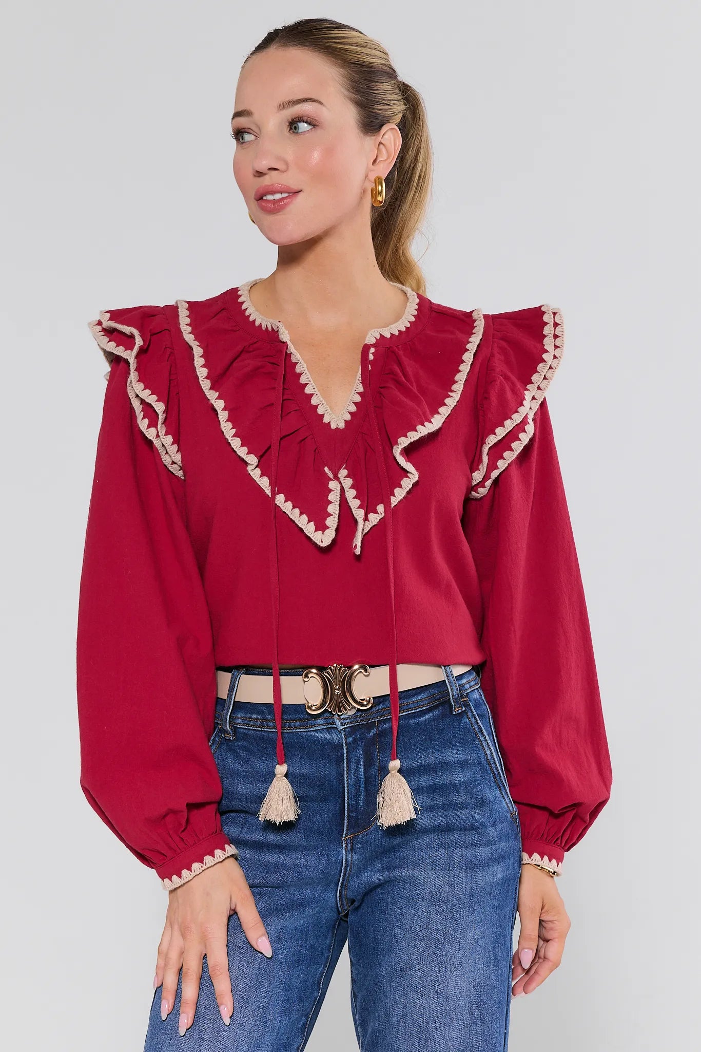 Woman wearing a red Viviana Top with ruffled details and blue jeans on a white background