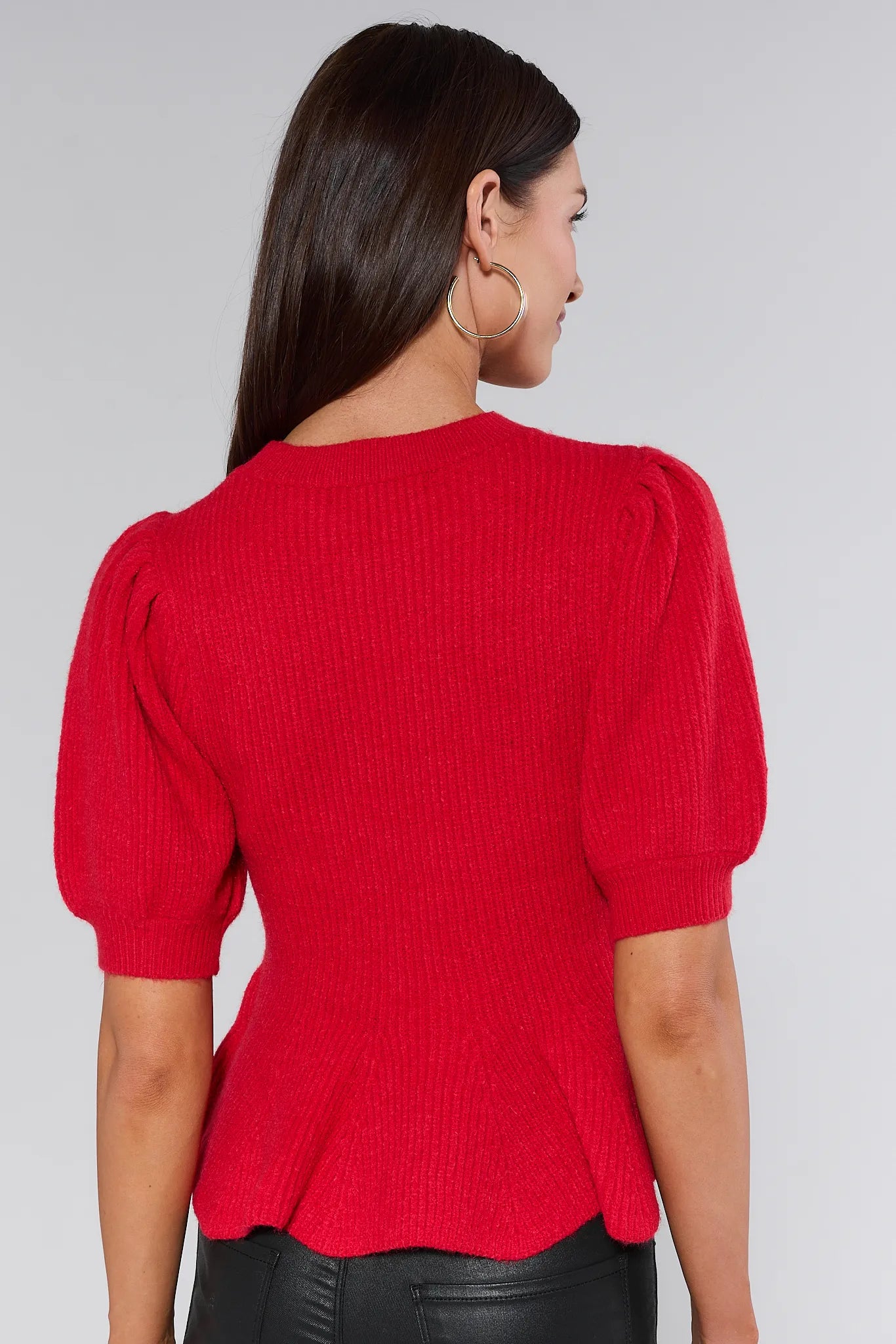 Woman wearing a red hillary sweater with puff sleeves against a plain background