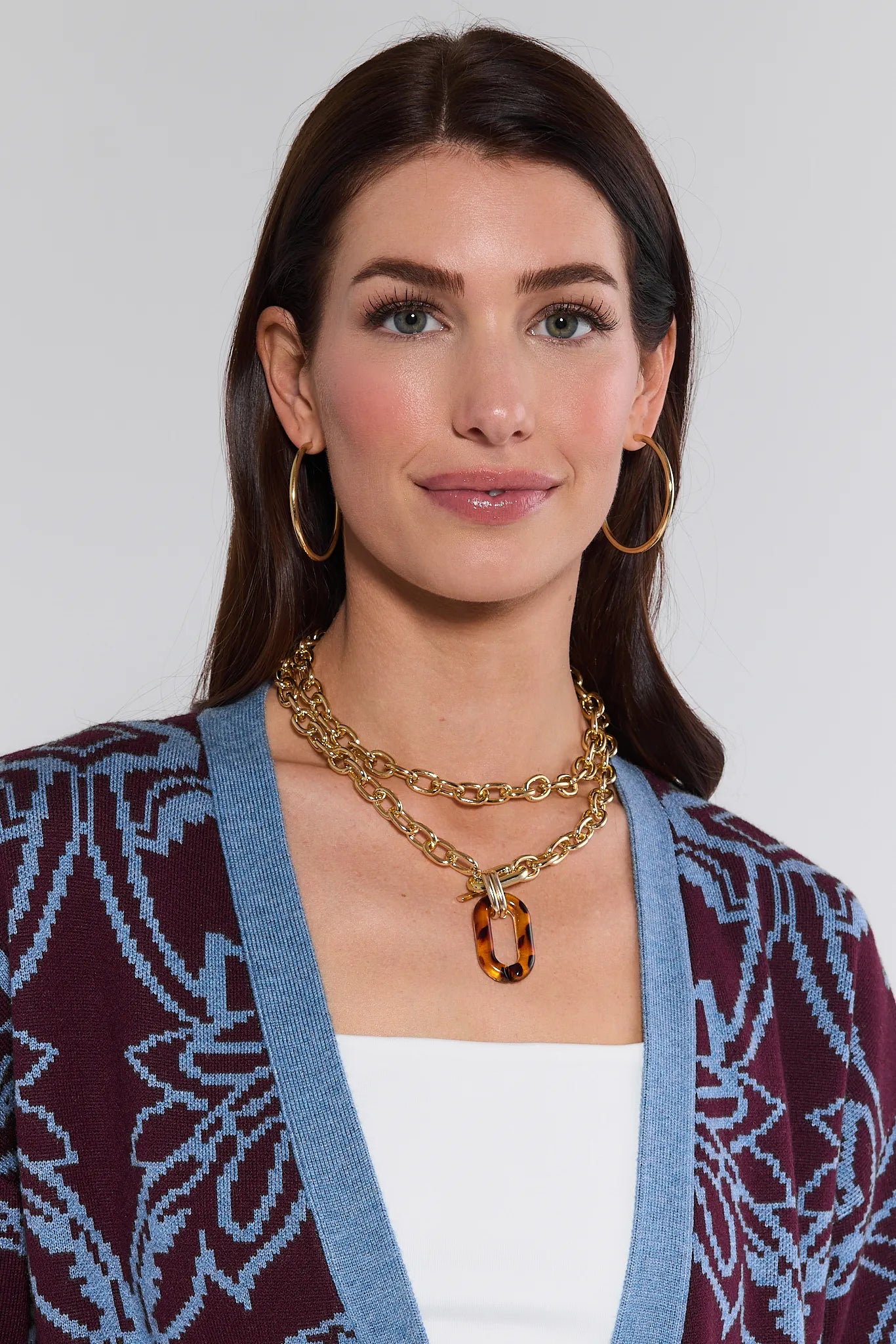 Woman wearing a patterned cardigan and gold Pippa Necklace against a plain background