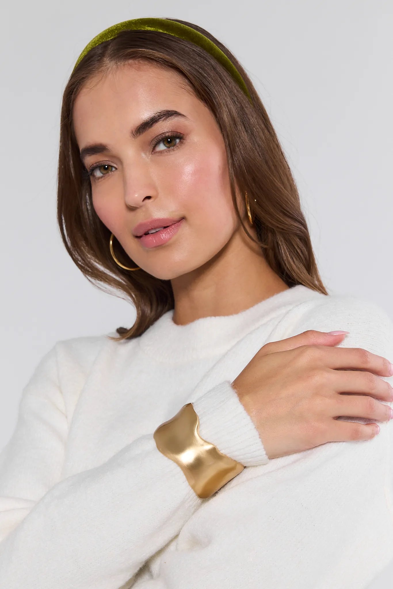 Woman wearing a white sweater with a gold Arden Bracelet against a light background
