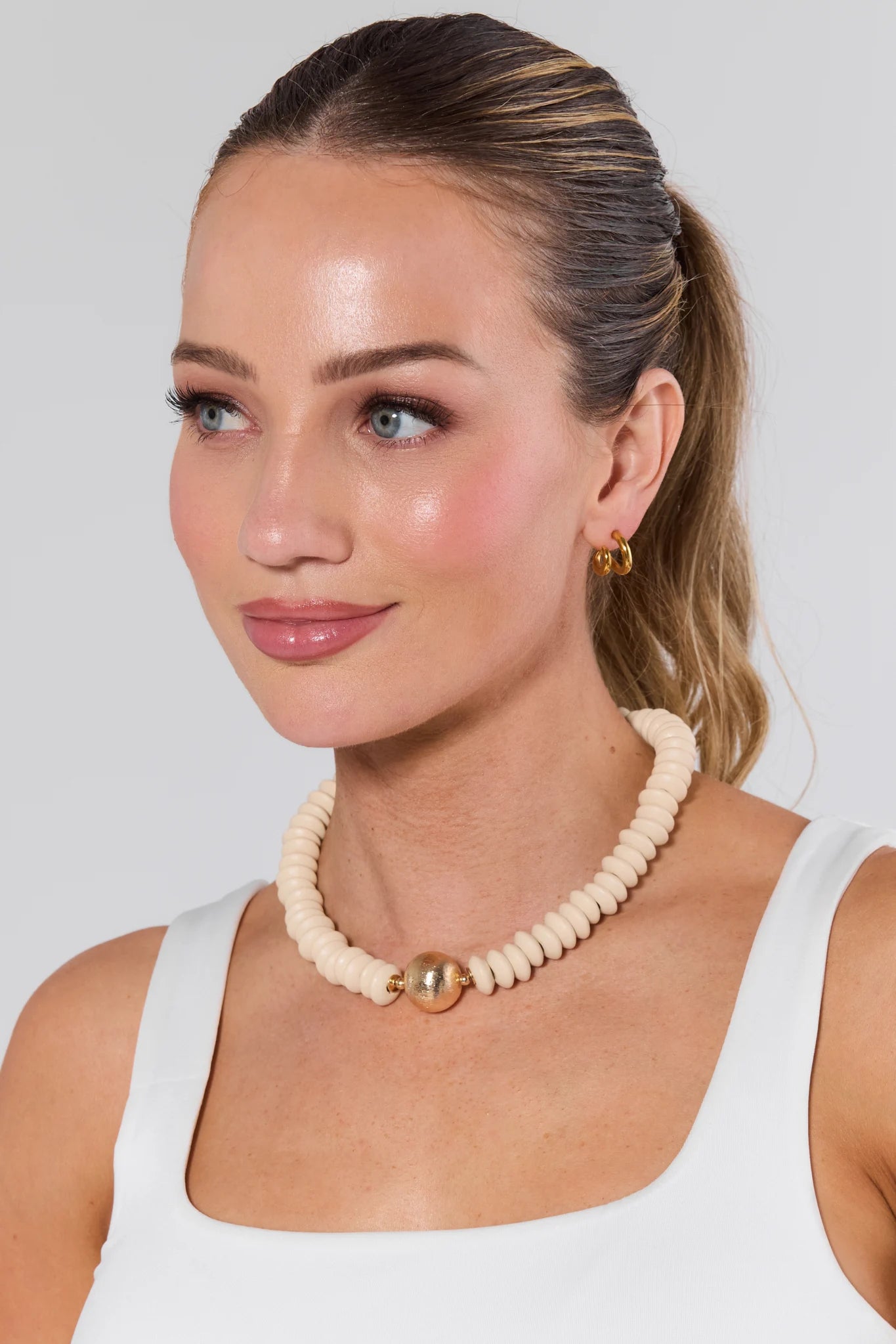 Woman wearing a beige beaded necklace with gold accents against a plain background