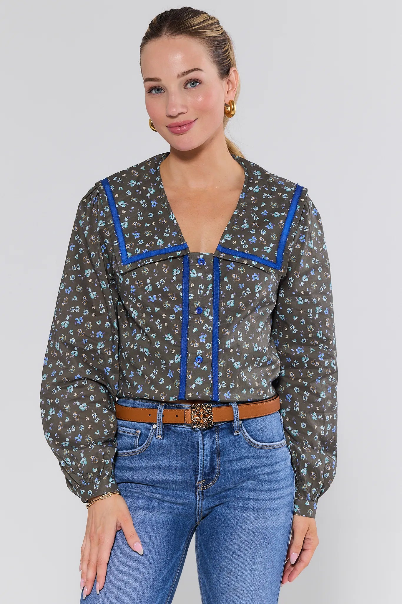 Woman wearing a patterned Carol Top
 with blue accents and jeans on a plain background