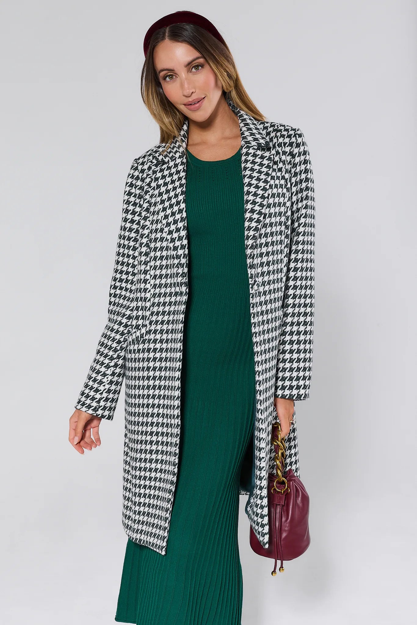 Woman wearing a Jonah Green Houndstooth Coat over a green dress with a plain background