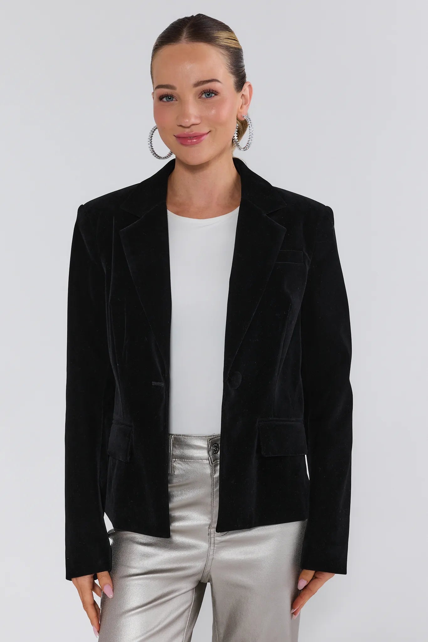 Woman wearing a black velvet blazer over a white top and silver pants on a white background