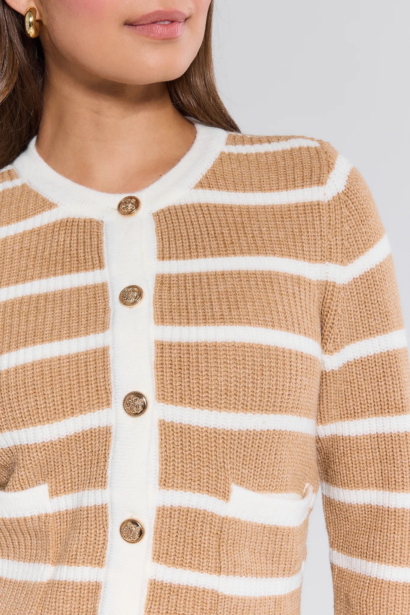 Close-up of a person wearing a beige and white striped Dayna Cardigan with gold buttons on a light gray background.