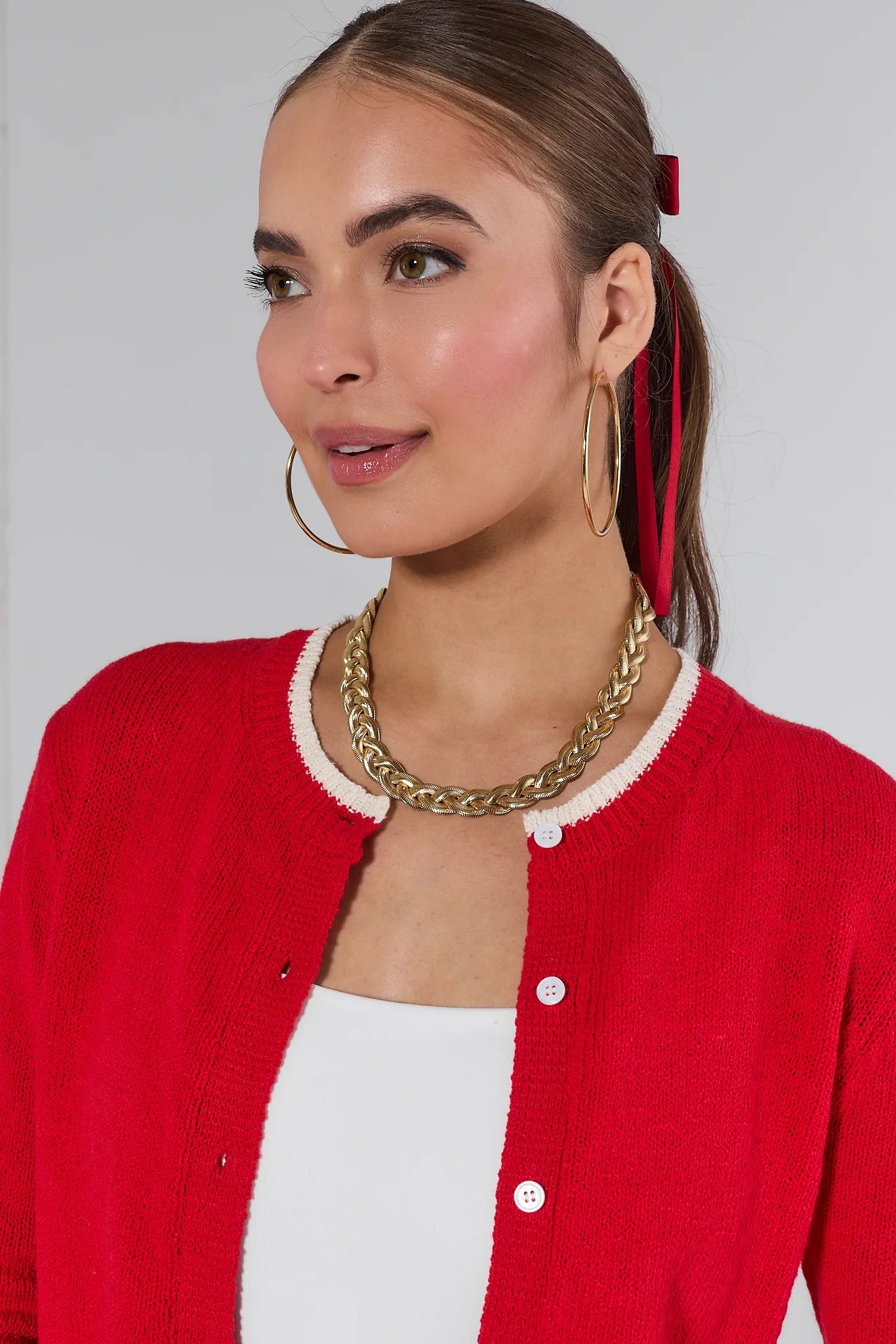 Woman wearing a red Karlie cardigan over a white top and green pants on a plain background