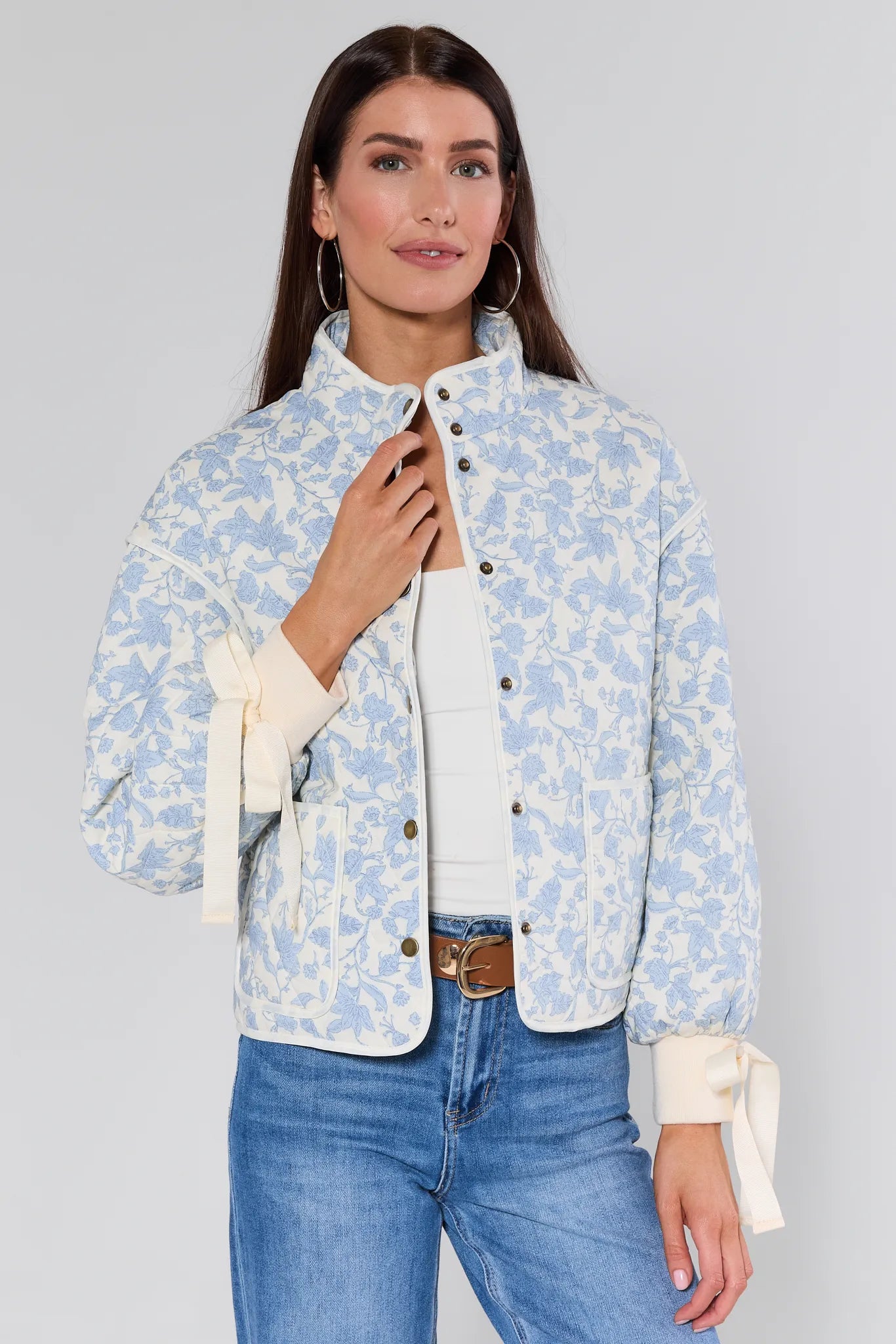 Woman wearing a light blue floral brett jacket over a white shirt with blue jeans on a gray background