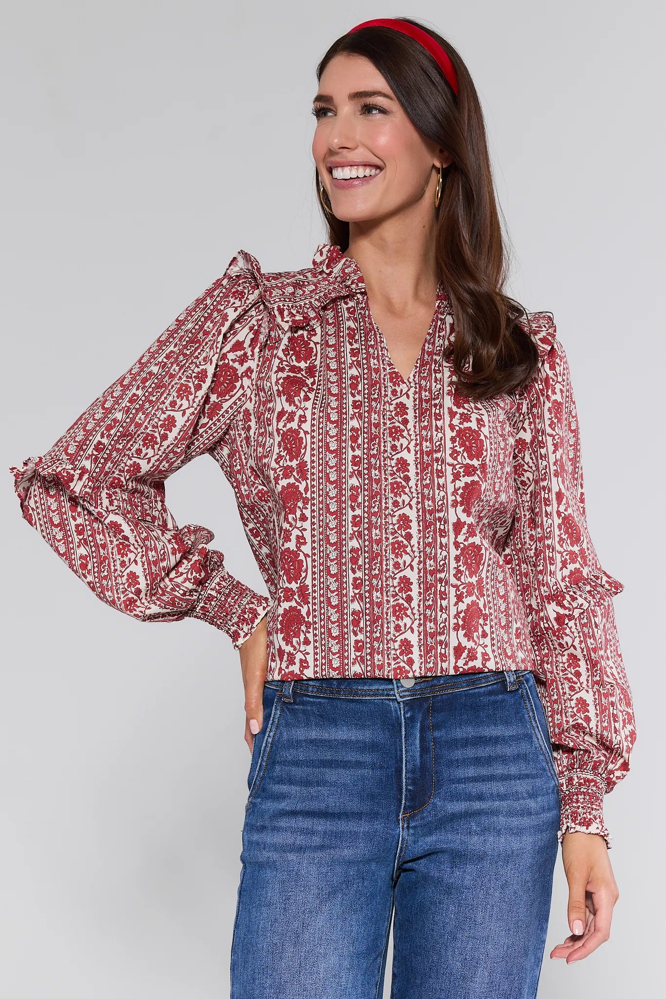 Woman wearing a red and white patterned Morgan Top with blue jeans on a gray background
