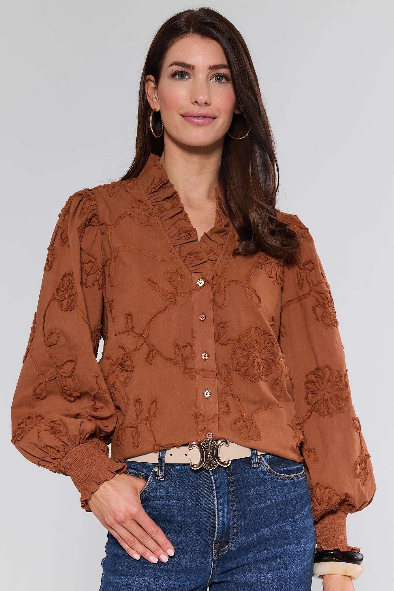 Woman wearing a brown floral Shaunda Top and blue jeans on a white background