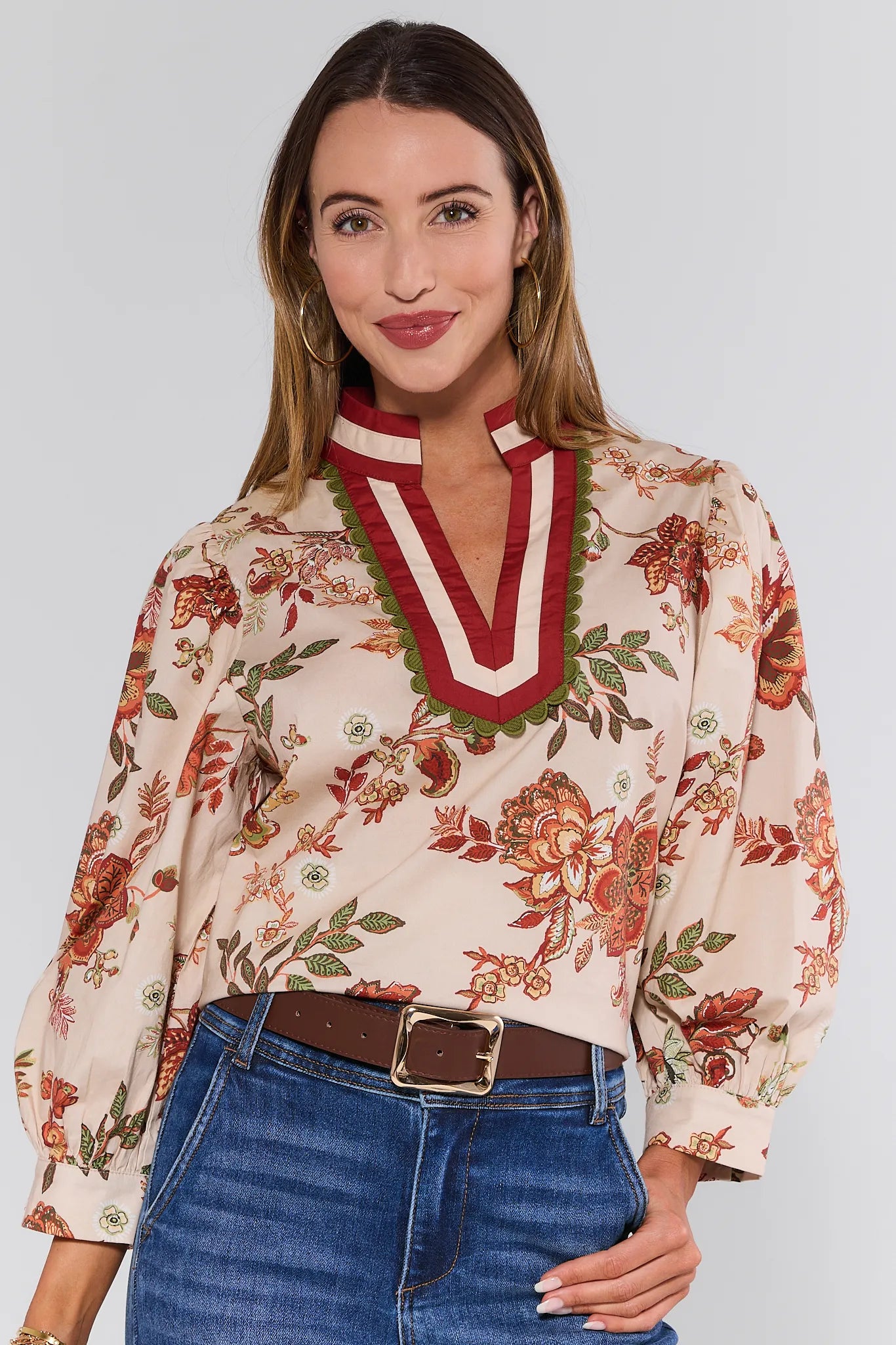 Woman wearing a floral Myra Top with a red collar and blue jeans on a white background