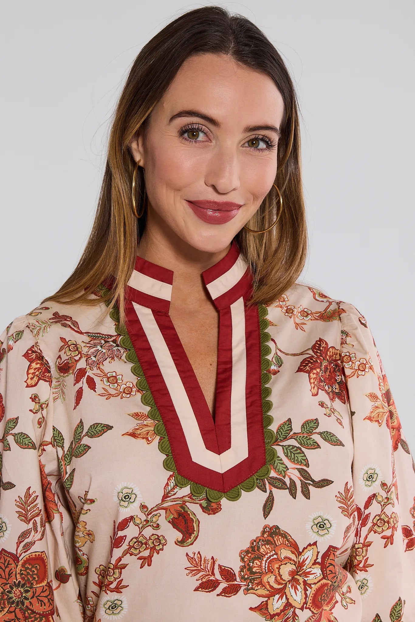 Woman wearing a floral Myra Top with a red and white collar against a plain background
