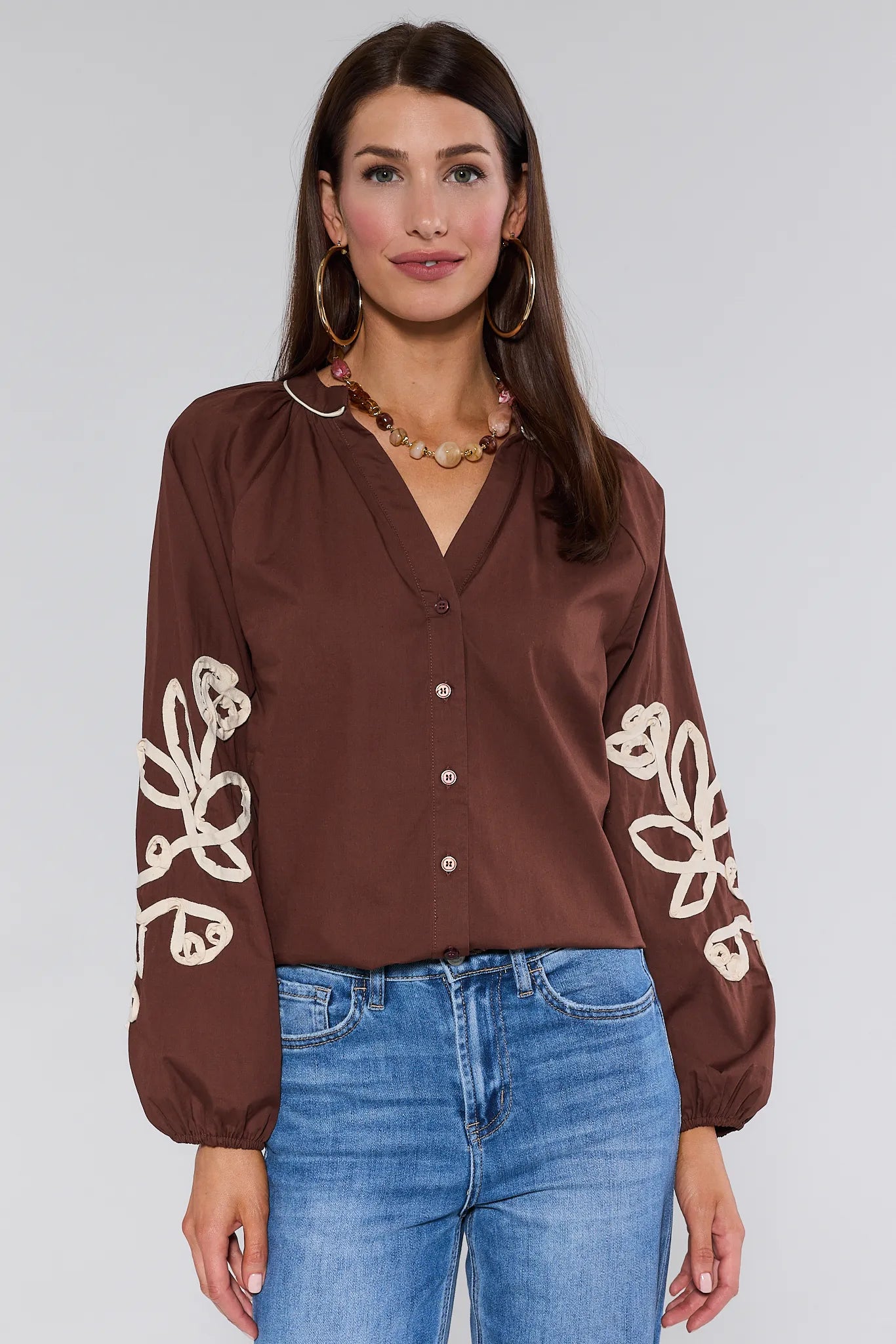 Woman wearing a brown Quinlan Top with floral patterns on long sleeves against a white background