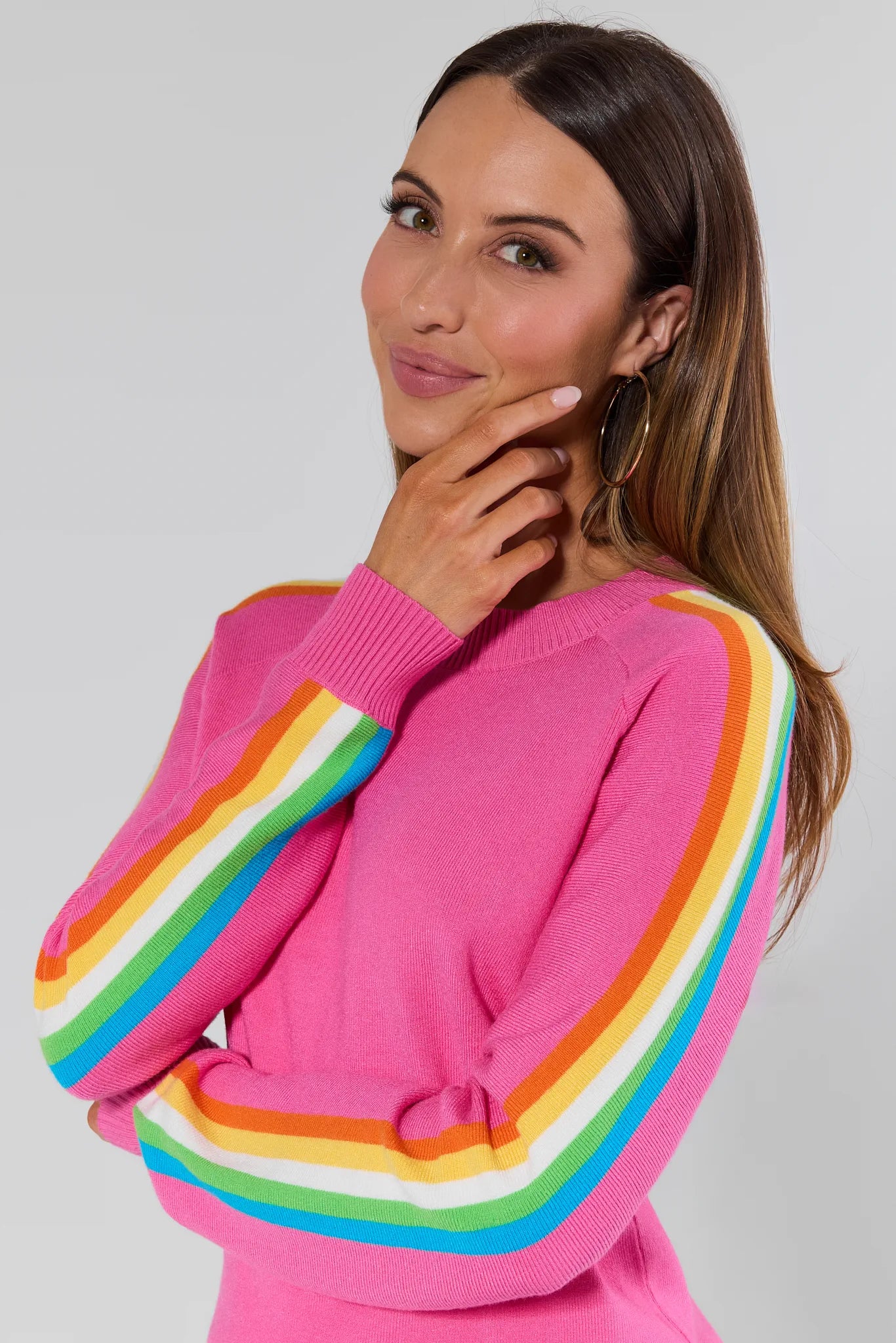 Woman wearing a pink sweater with rainbow sleeves against a plain background Khloe Pink Striped Sleeve Sweater