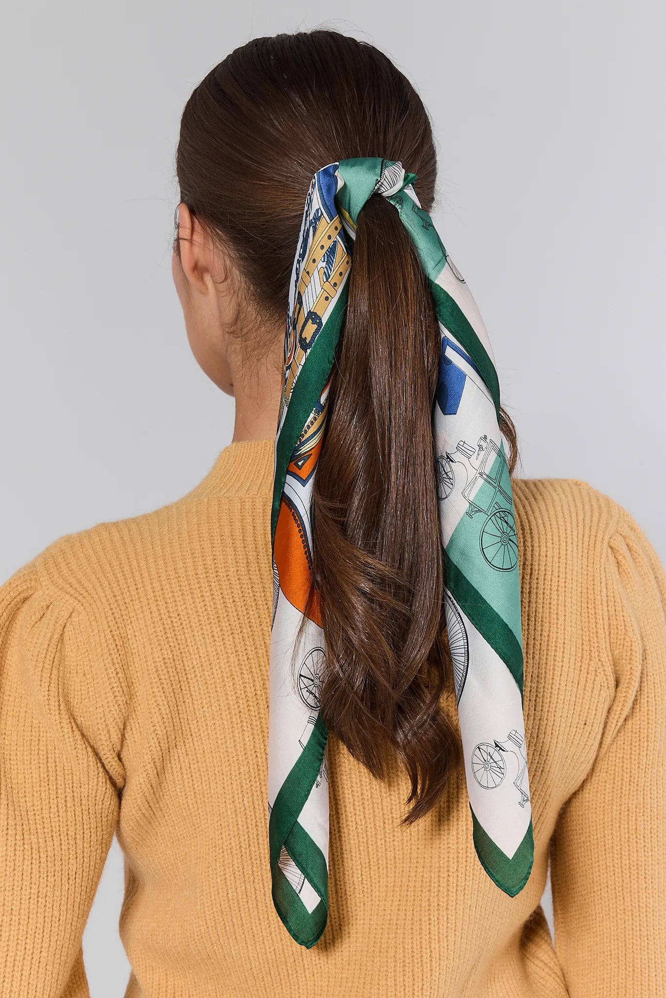 Person wearing a patterned green Lindsay Scarf in their hair against a plain background