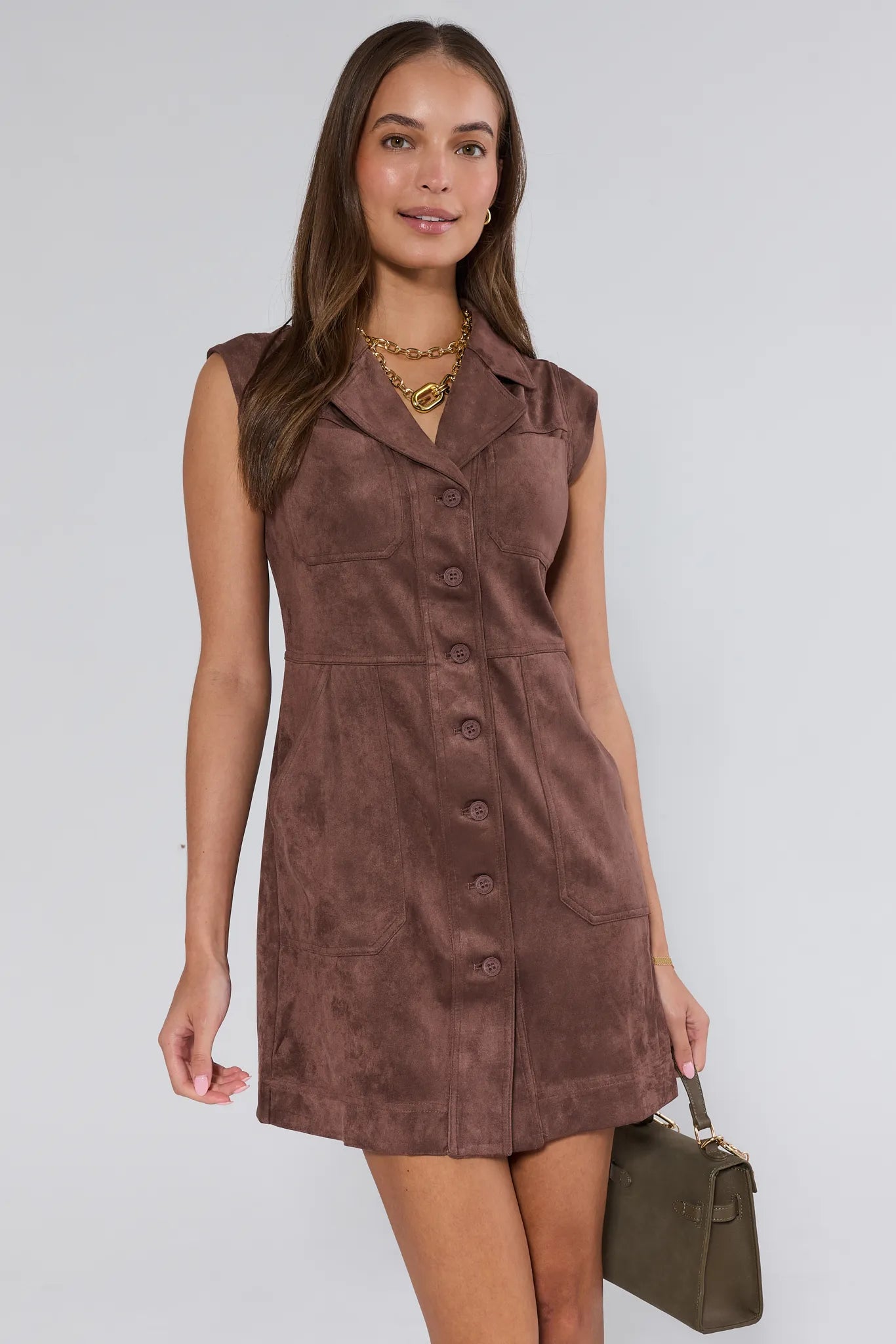 Woman wearing a brown suede Kenzie Dress holding a matching handbag against a white background