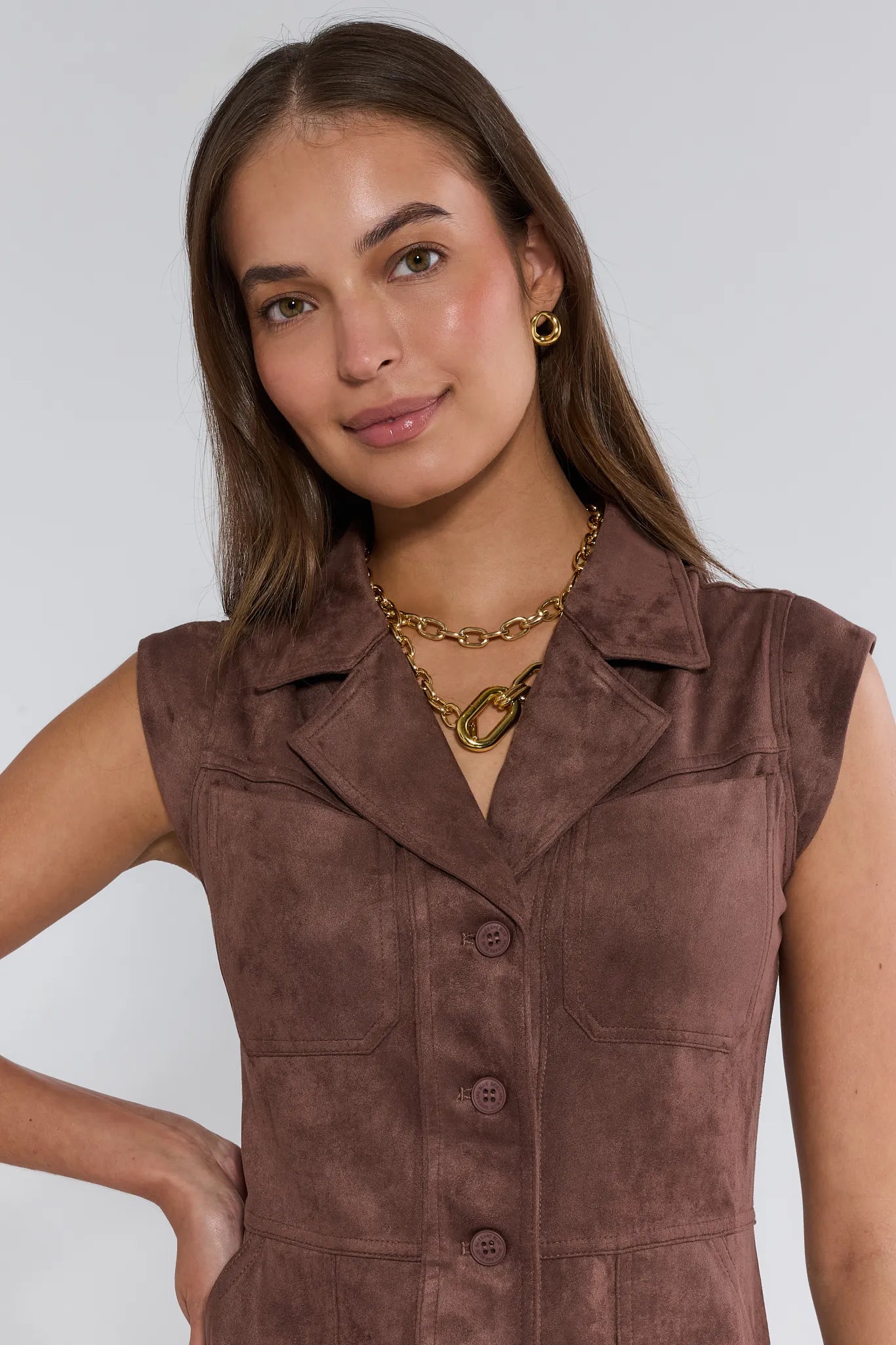 Woman wearing a brown suede Kenzie Dress with gold jewelry against a plain background