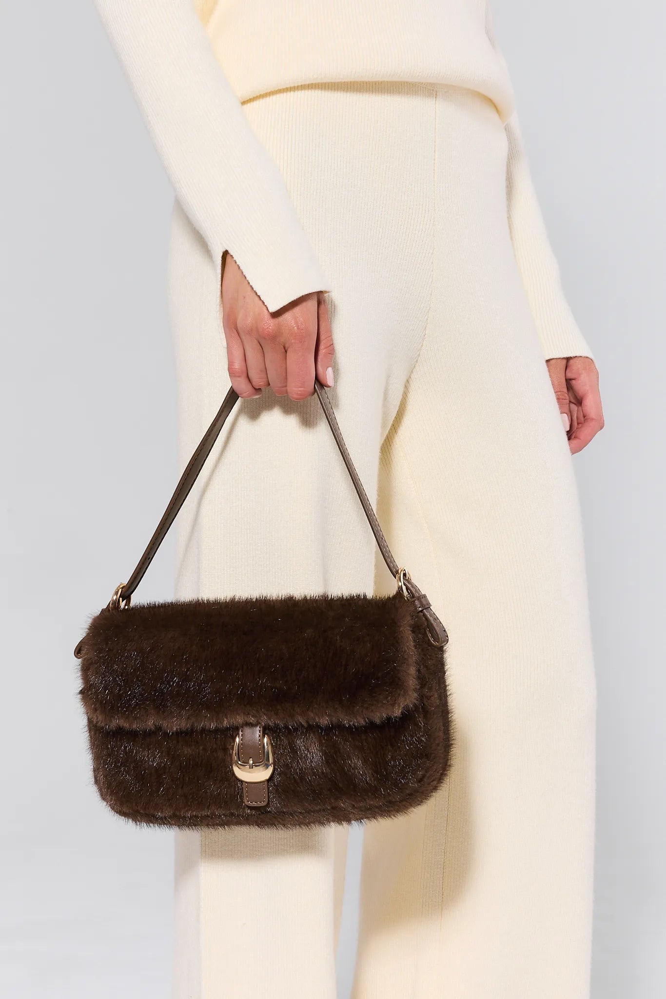 Brown fur Gloria Bag held by a person wearing a white coat against a light gray background