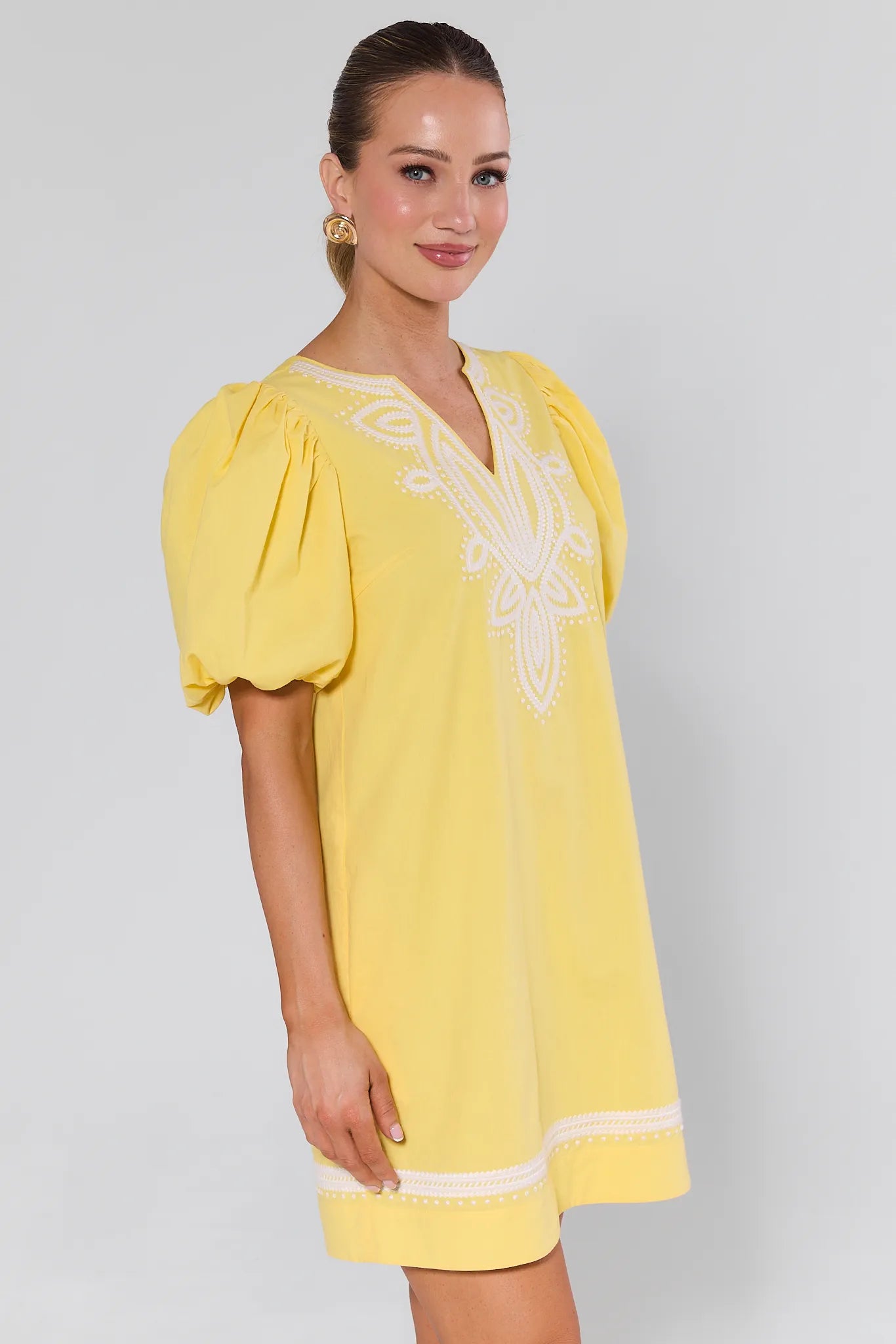 Woman wearing a yellow dress with white embroidery on a plain background Roxanne Dress Yellow