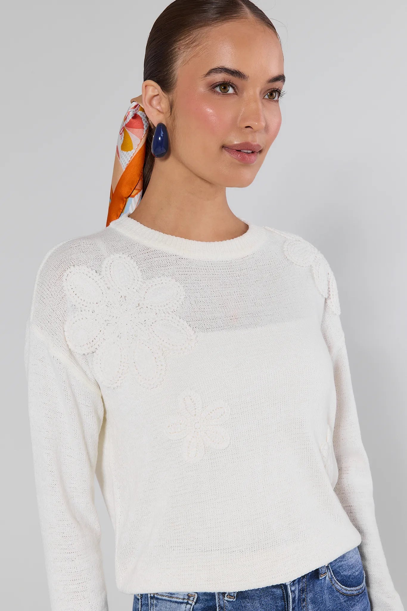 Woman wearing a Violet Cream Summer Sweater and blue jeans with colorful scarf against a gray background