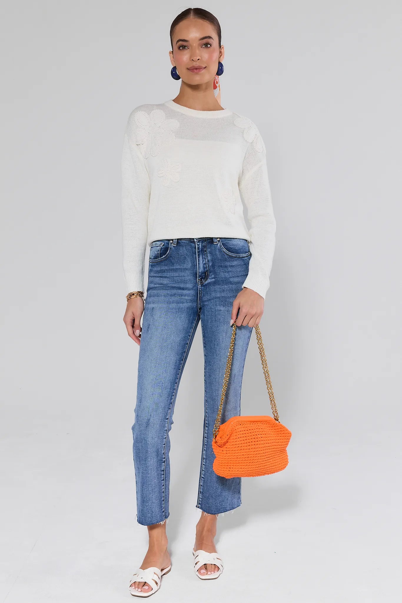 Woman wearing a Violet Cream Summer Sweater and blue jeans, holding an orange handbag on a plain background