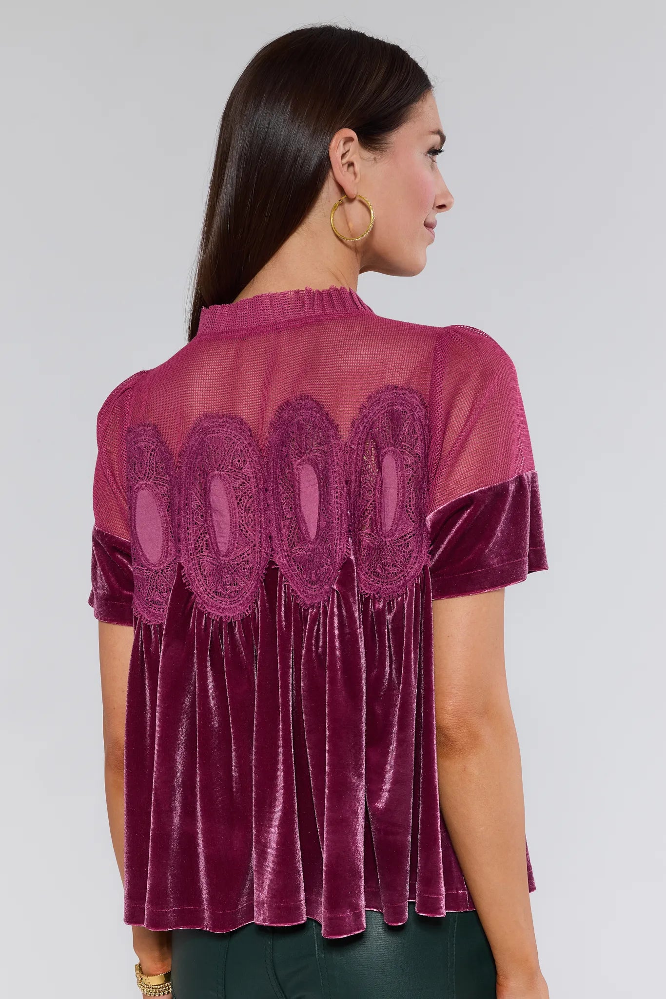 Woman wearing a burgundy gabrielle velvet top with lace details on a plain background