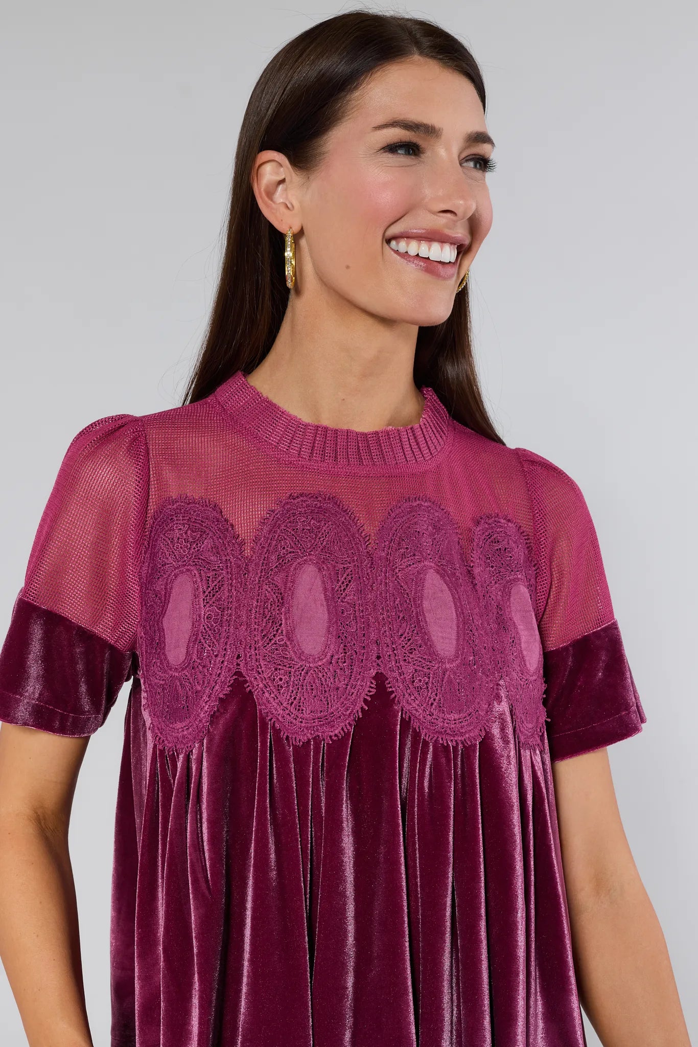 Woman wearing a burgundy gabrielle velvet top with lace details on a plain background