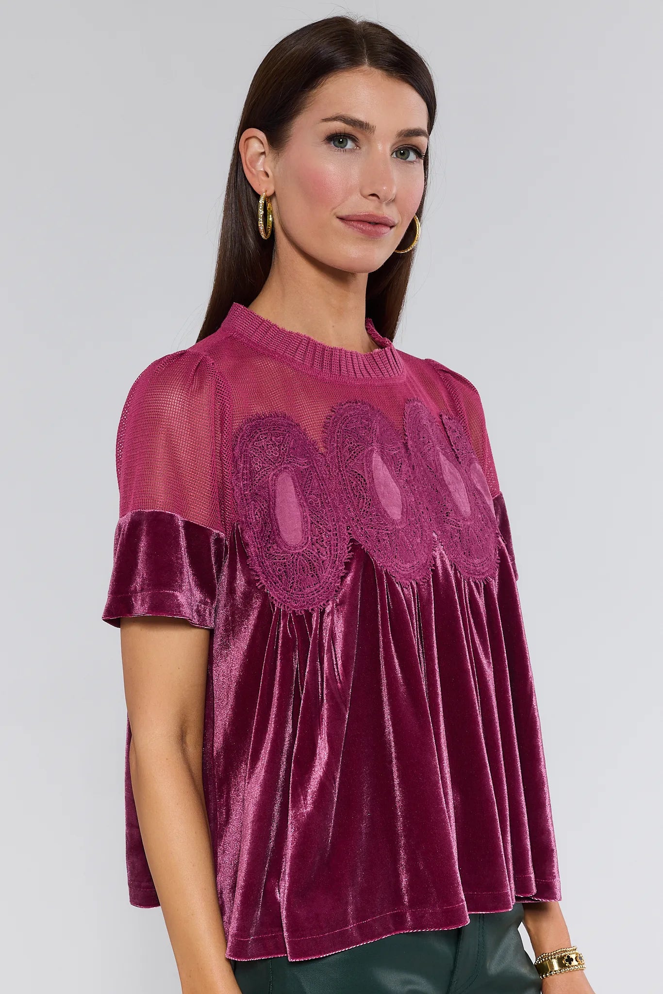 Woman wearing a burgundy gabrielle velvet top with lace details on a plain background