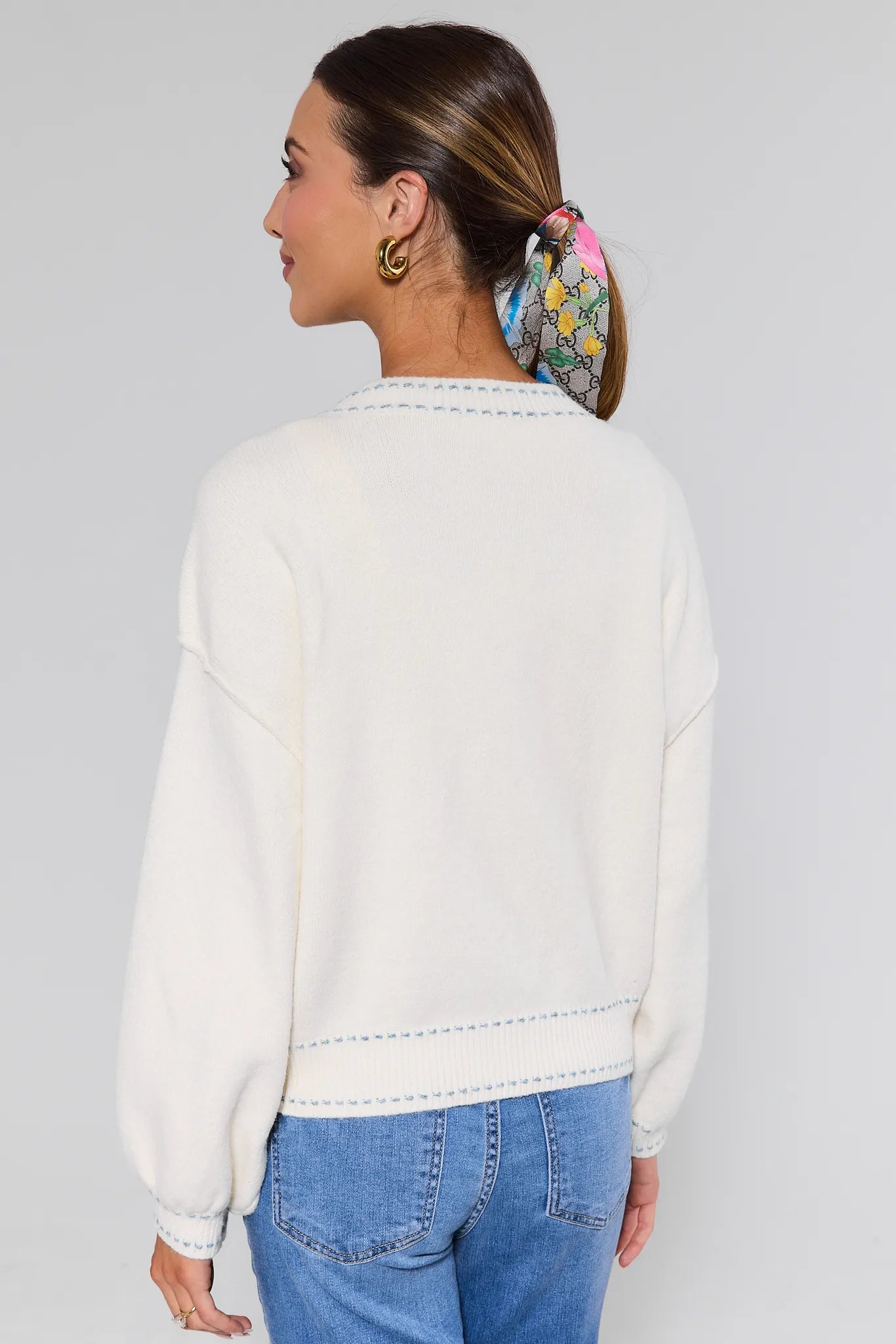 Woman wearing a white sweatshirt and blue jeans with a colorful headband on a plain background