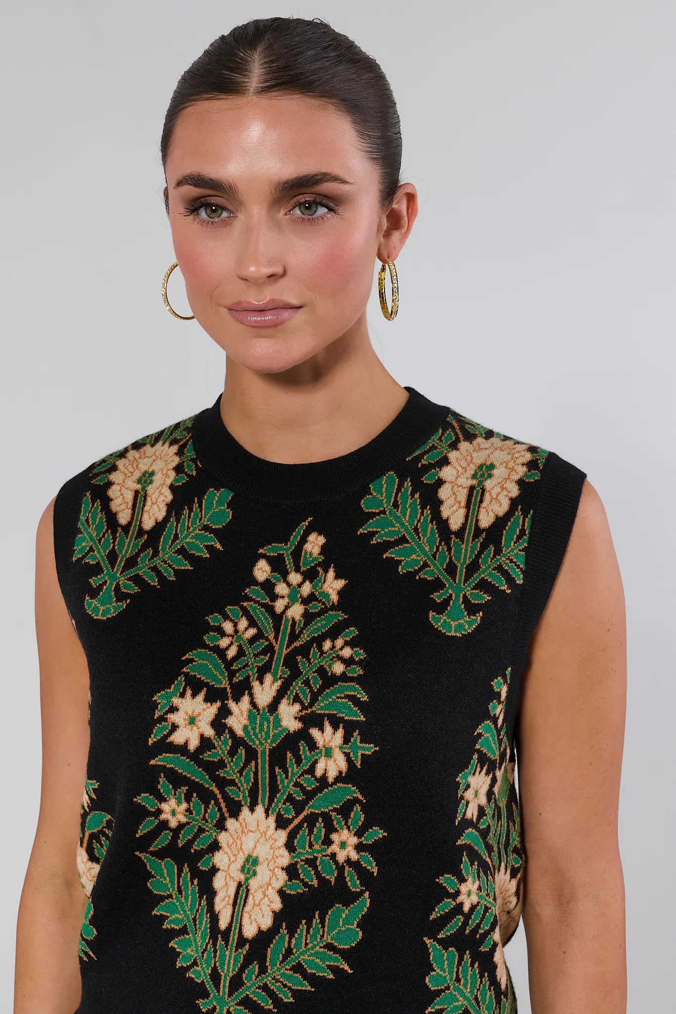 Woman wearing a black sleeveless Edie Sweater with floral embroidery on a plain background