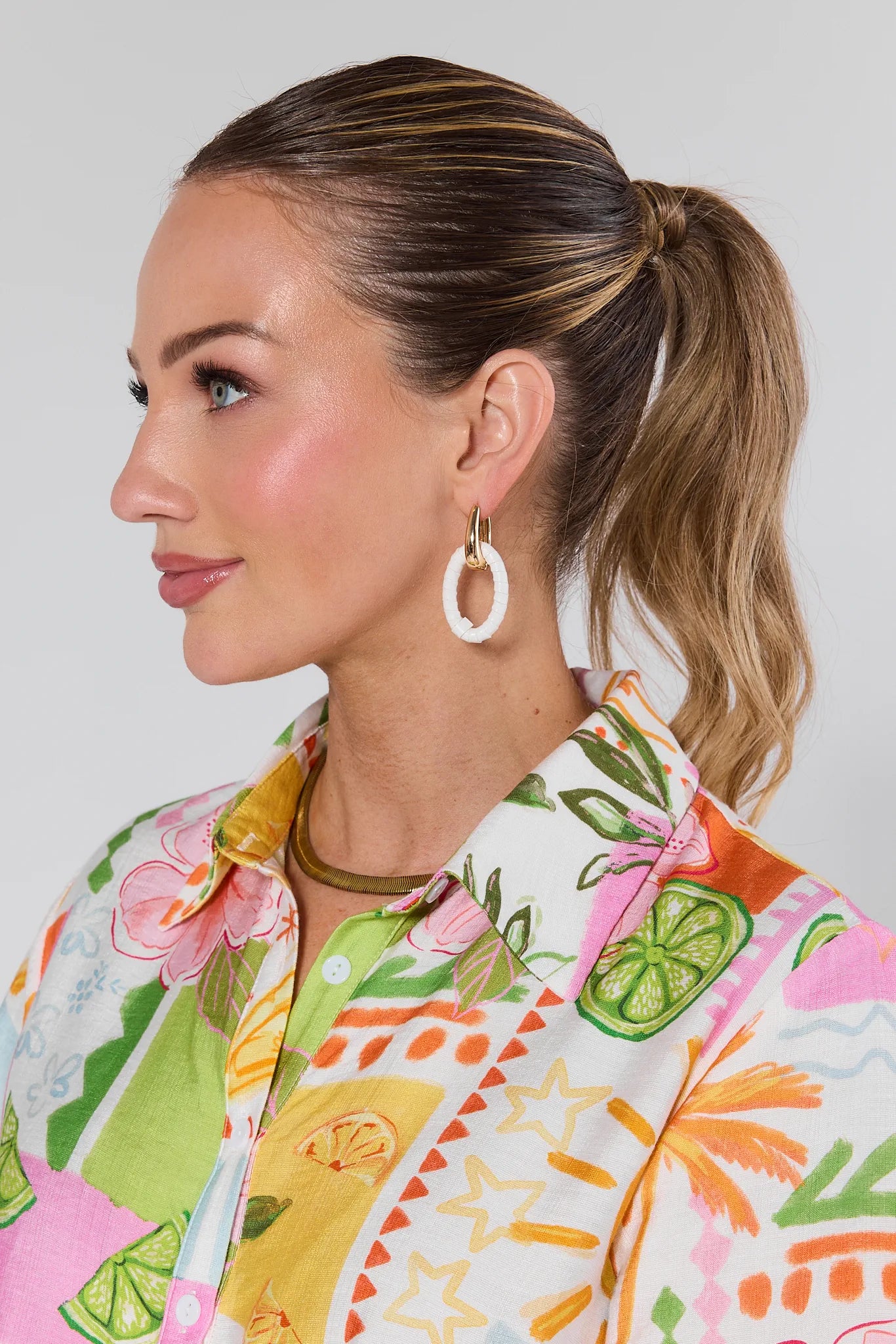 Woman wearing a colorful floral shirt and Raleigh Gold Drop Earrings with a plain background