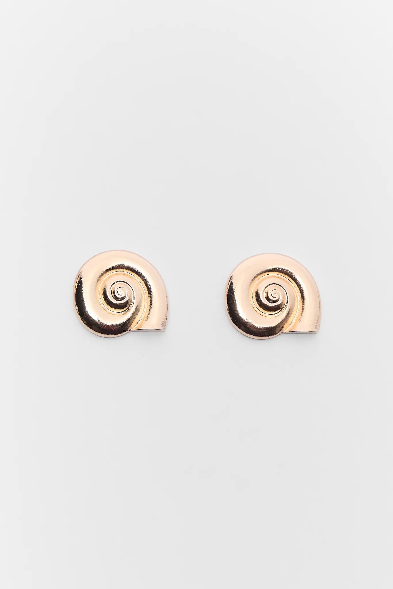 Pair of spiral-shaped Mara Gold Seashell Earrings on a light gray background
