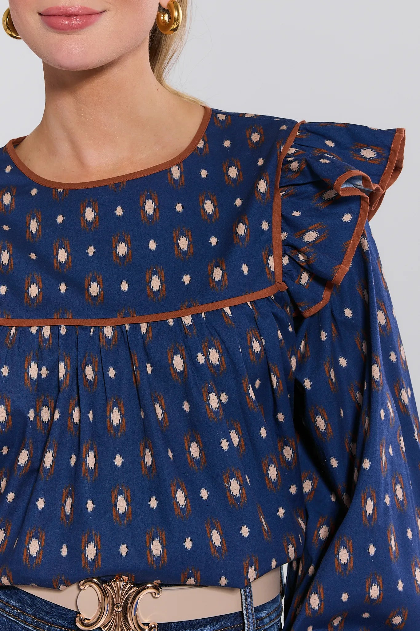 Close-up of a blue patterned Cleo Top with brown trim on a plain background