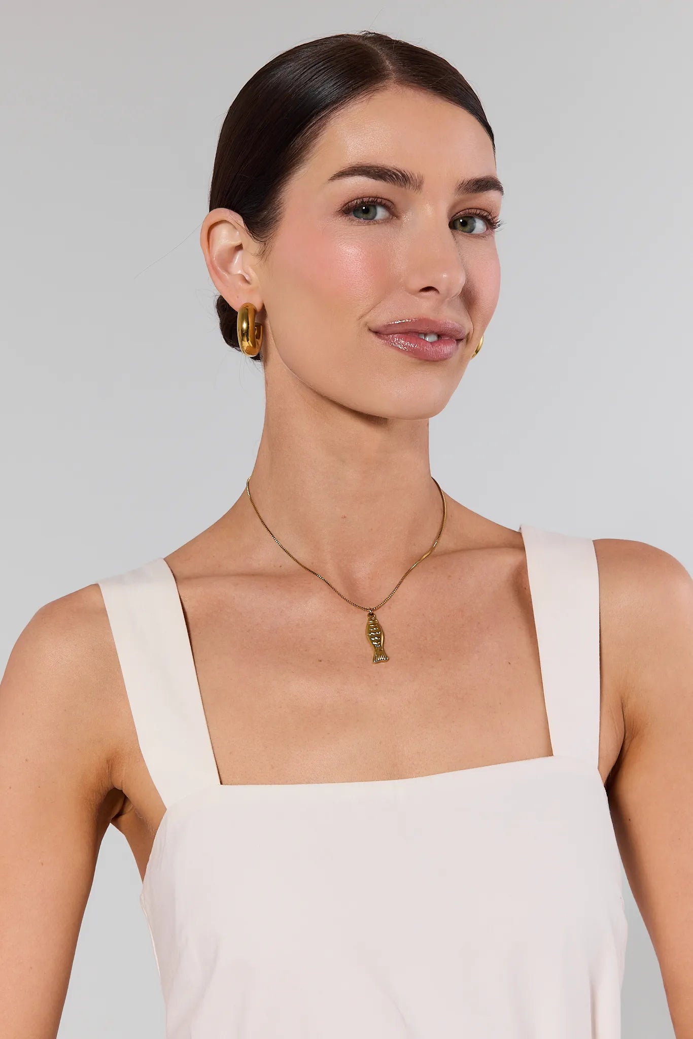 Woman wearing a gold necklace and earrings against a plain background