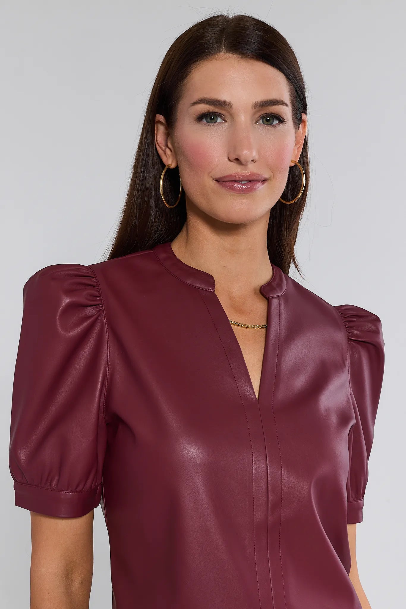 Woman wearing a burgundy leather Ariana Top with puff sleeves against a plain background