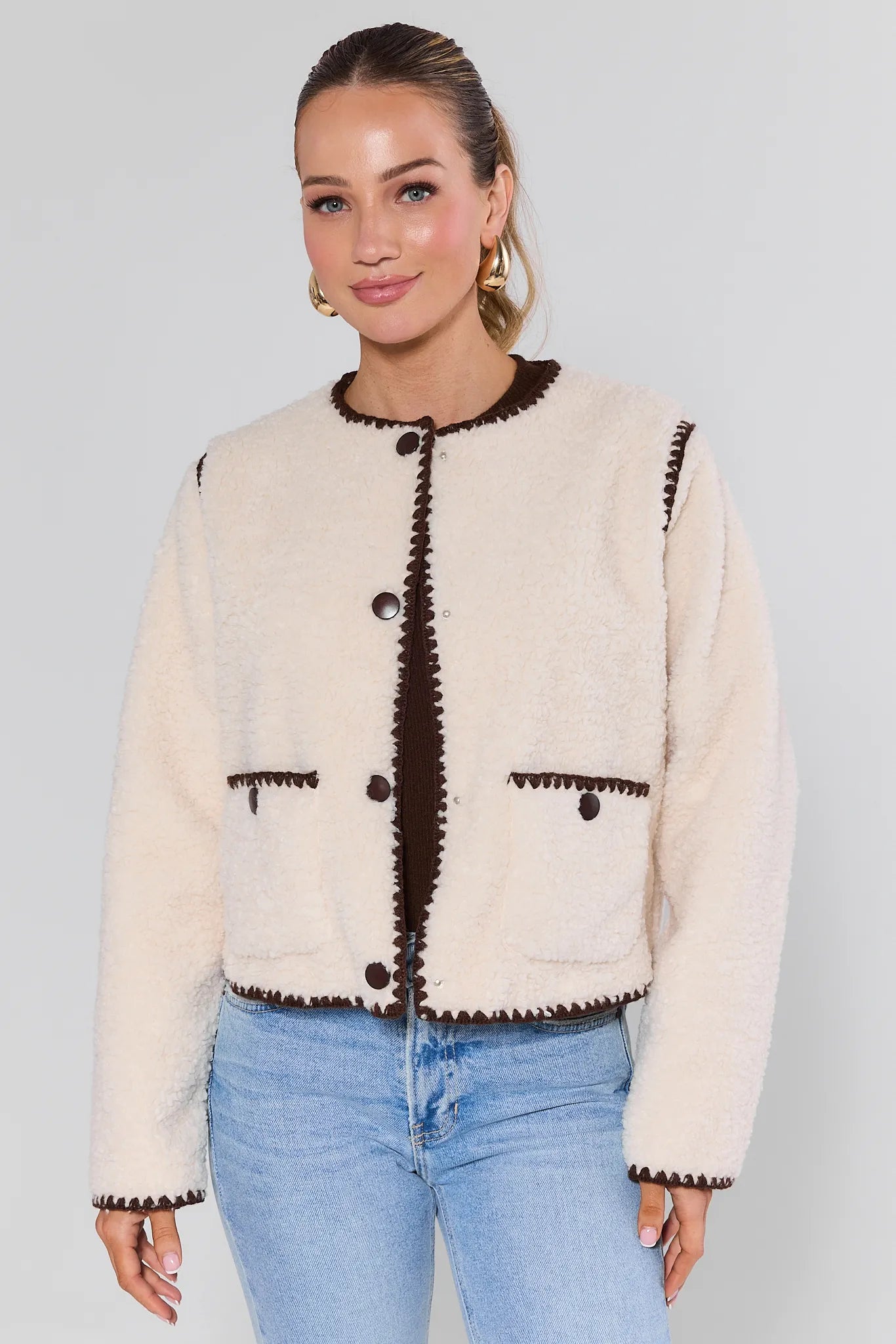 Woman wearing a Michelle Ivory Sherpa Jacket with brown trim against a plain background