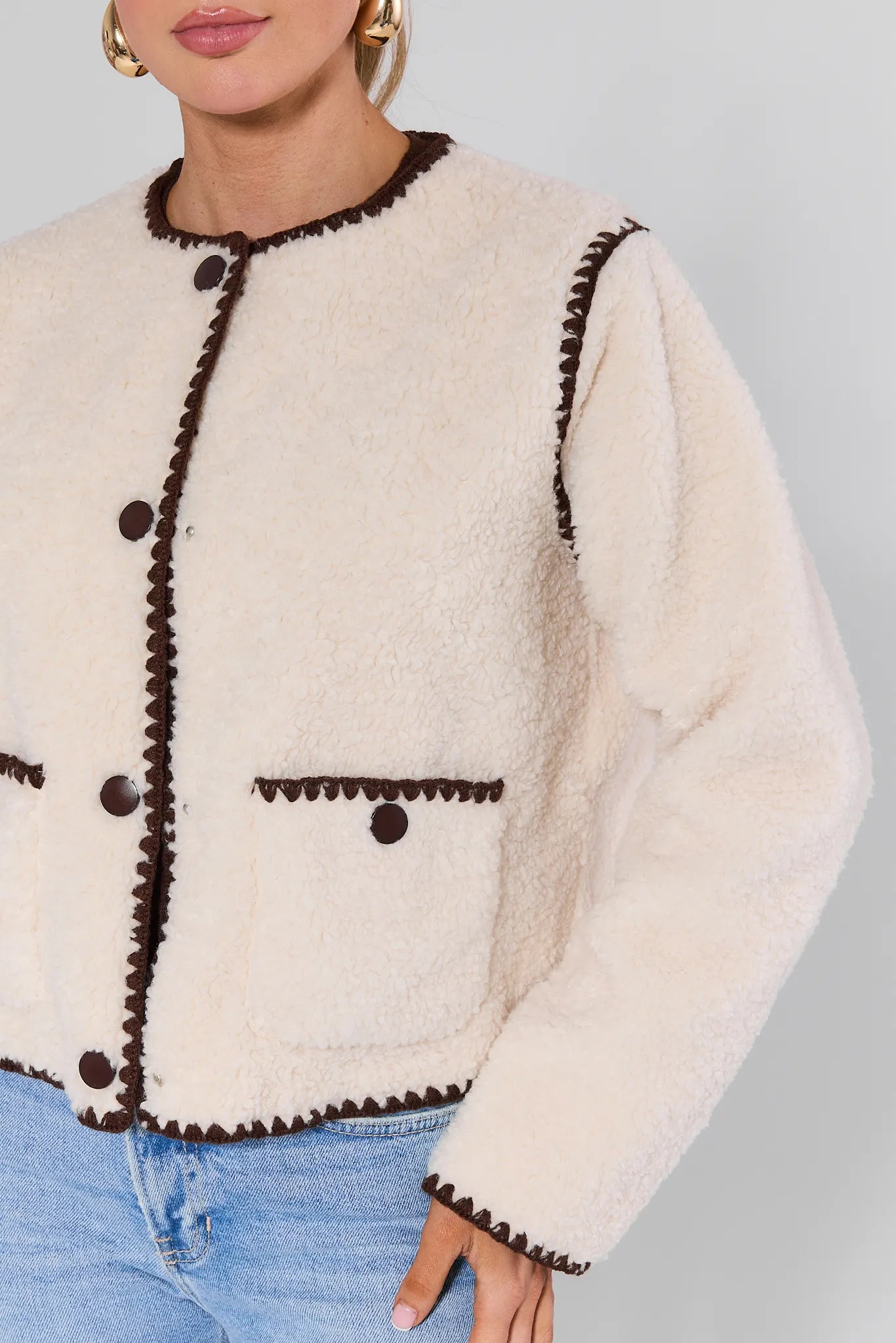 Woman wearing a Michelle Ivory Sherpa Jacket with brown trim against a plain background