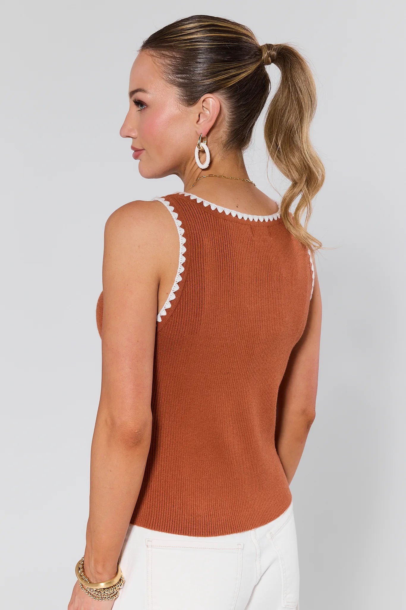 Woman wearing a Regan Brown Whipstitched Top with white trim and earrings on a plain background