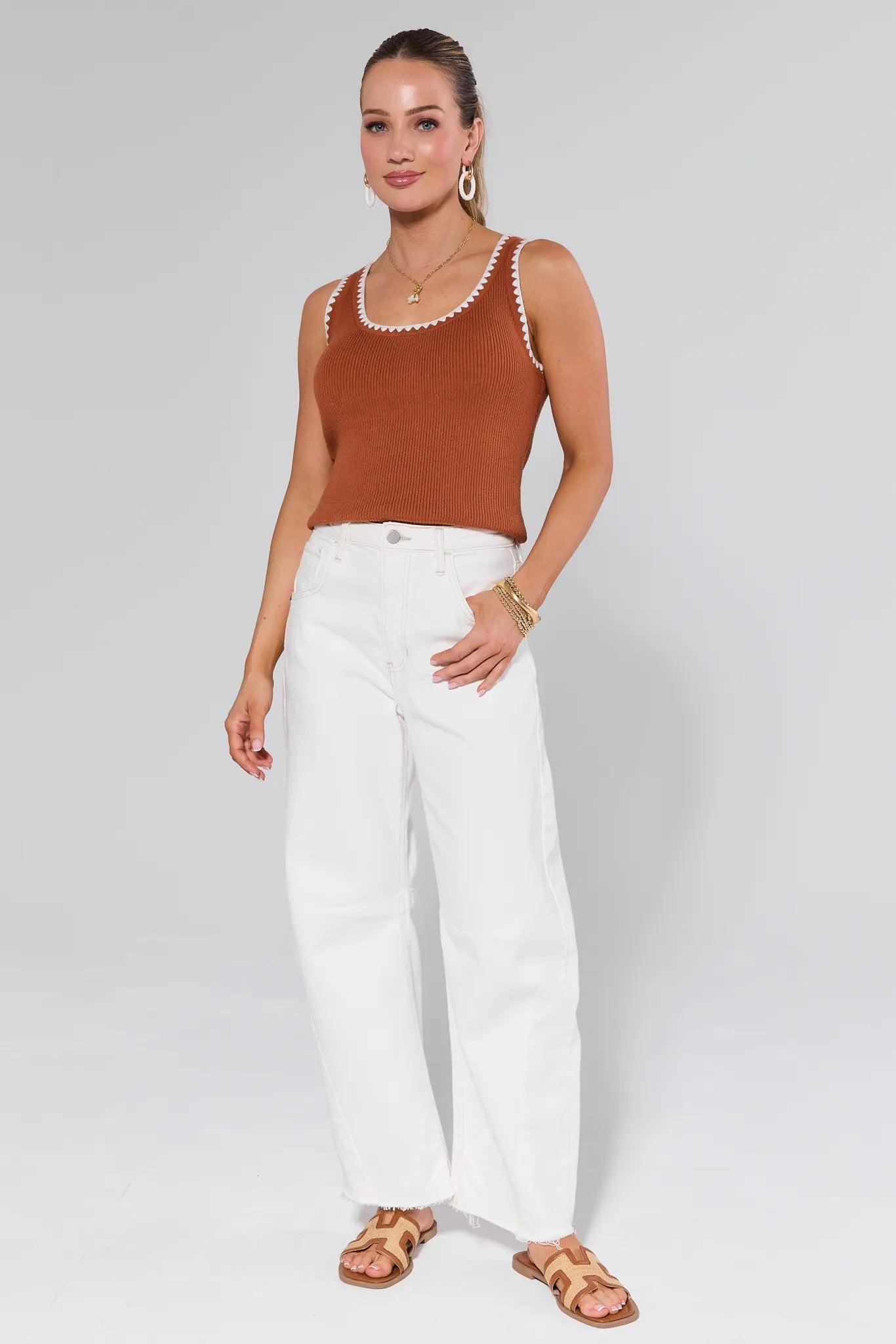 Woman wearing a Regan Brown Whipstitched Top and white pants on a plain background