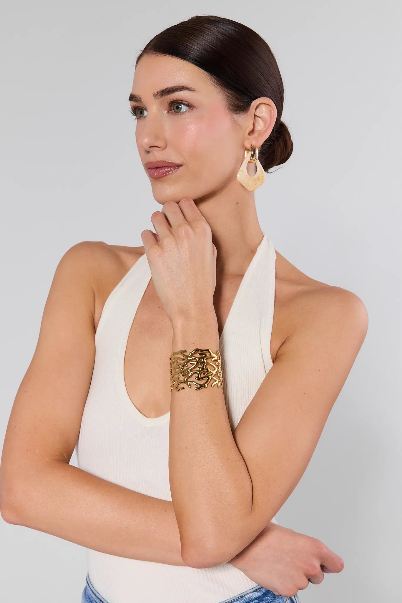 Woman wearing gold jewelry including earrings and a bracelet on a plain background