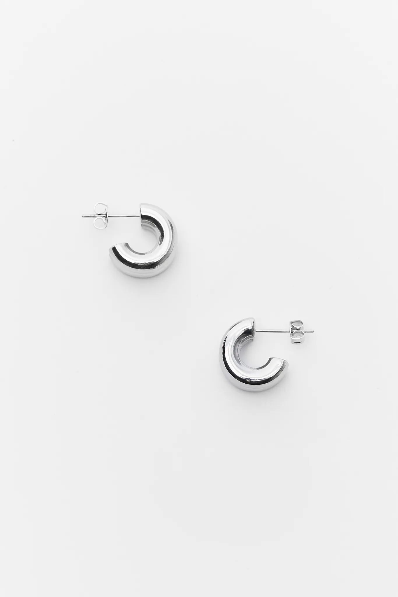 Pair of silver hoop earrings on a white background Emma Silver Huggie Earrings