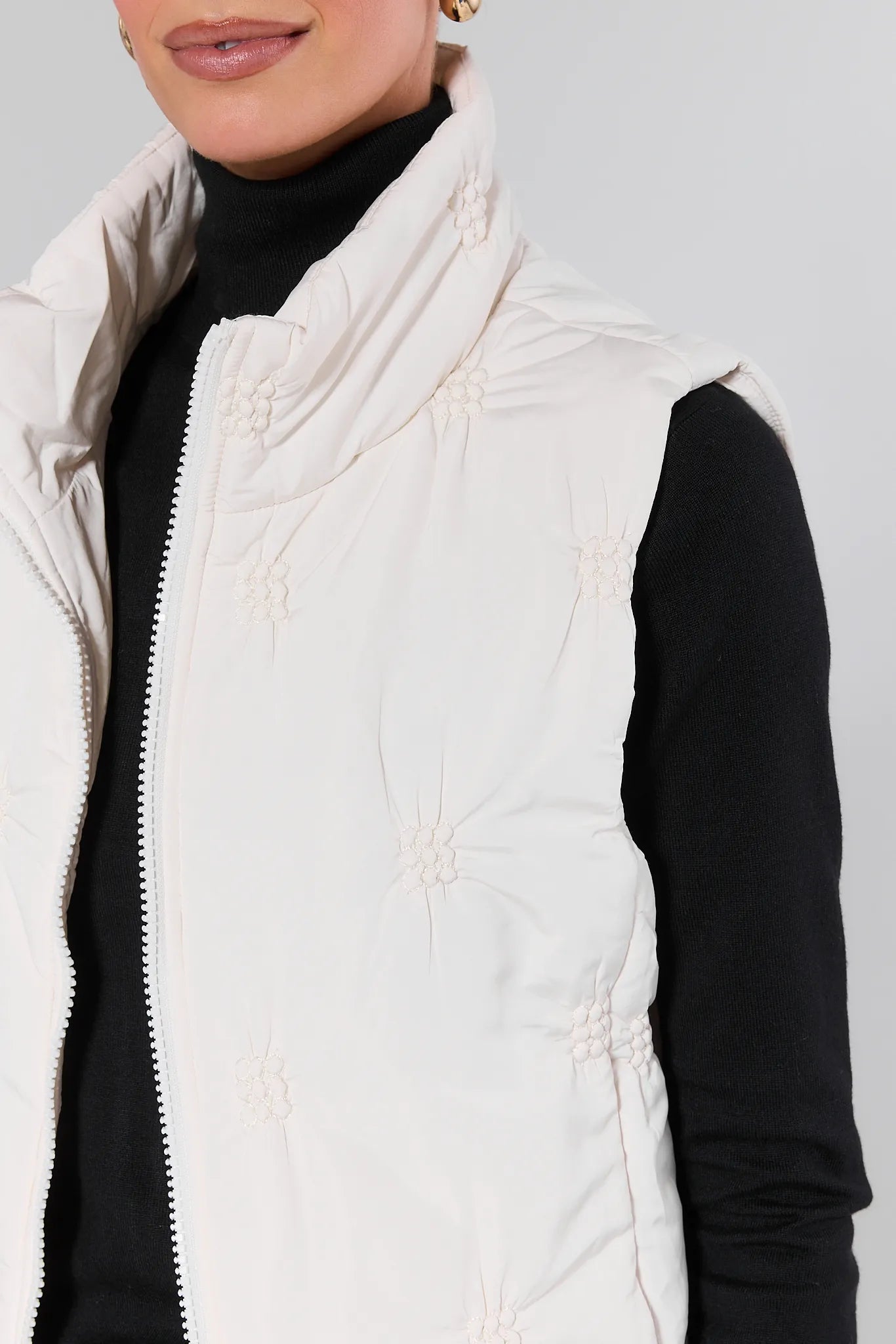 Woman wearing a Tiffany White Embroidered Puffer Vest over a black top on a gray background
