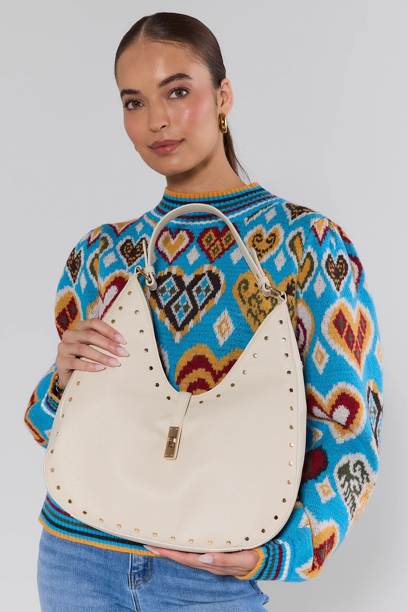 Woman holding a Olivia Cream Slouchy Shoulder Bag wearing a colorful sweater with geometric patterns.