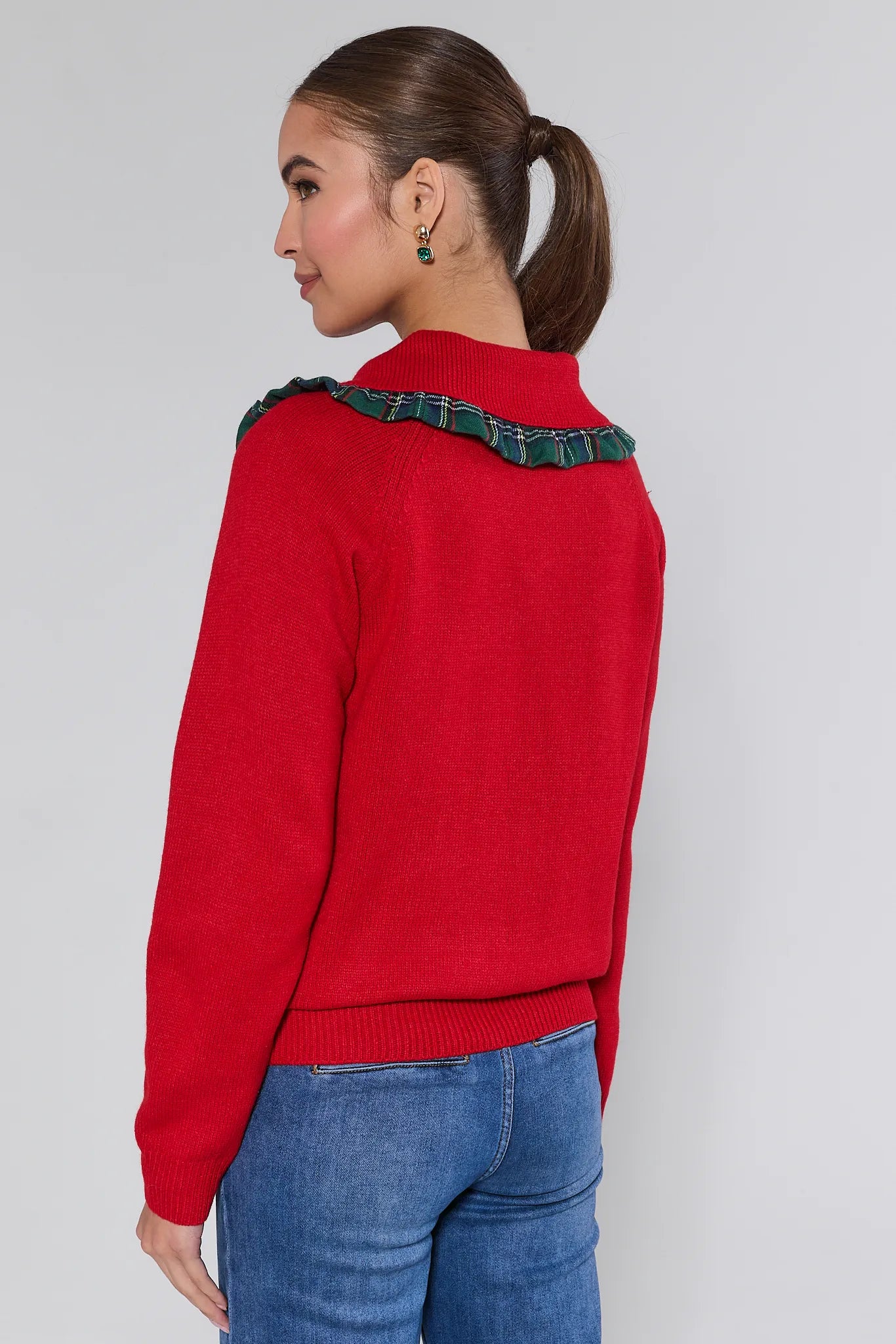 Woman wearing a red sweater with green trim on a plain background