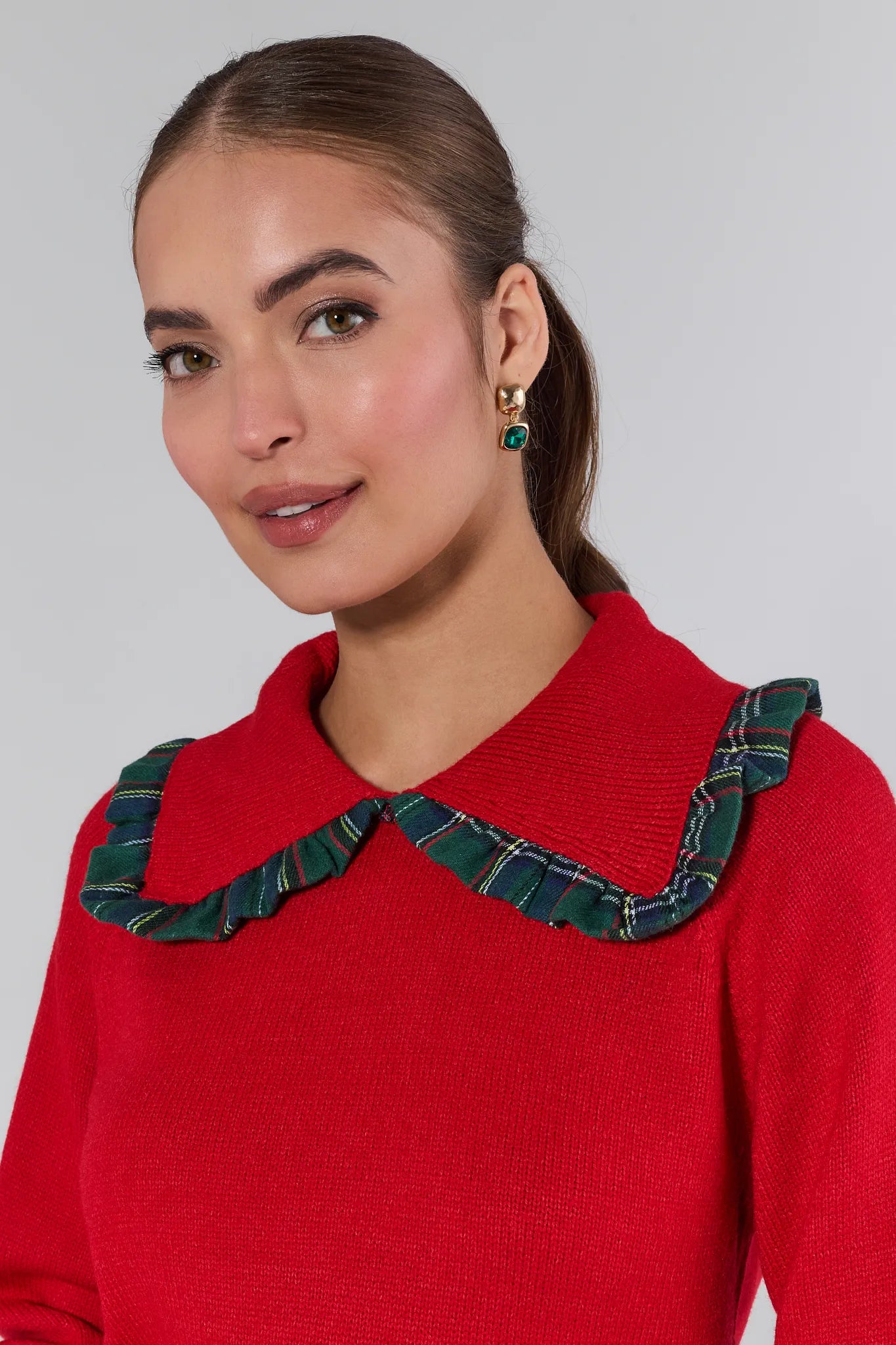 Woman wearing a red sweater with a green plaid collar against a gray background