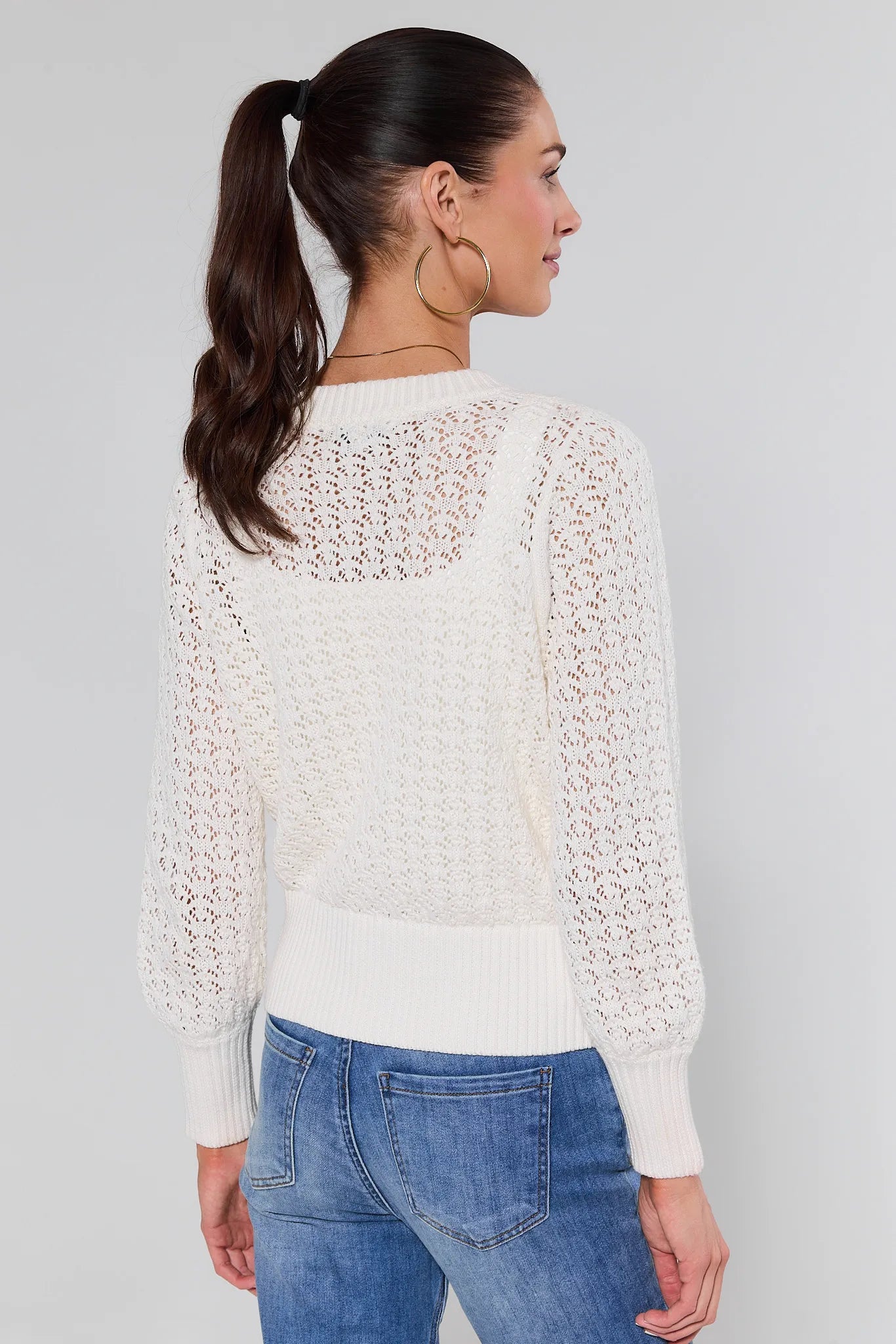 Woman wearing a white textured sweater and blue jeans against a gray background