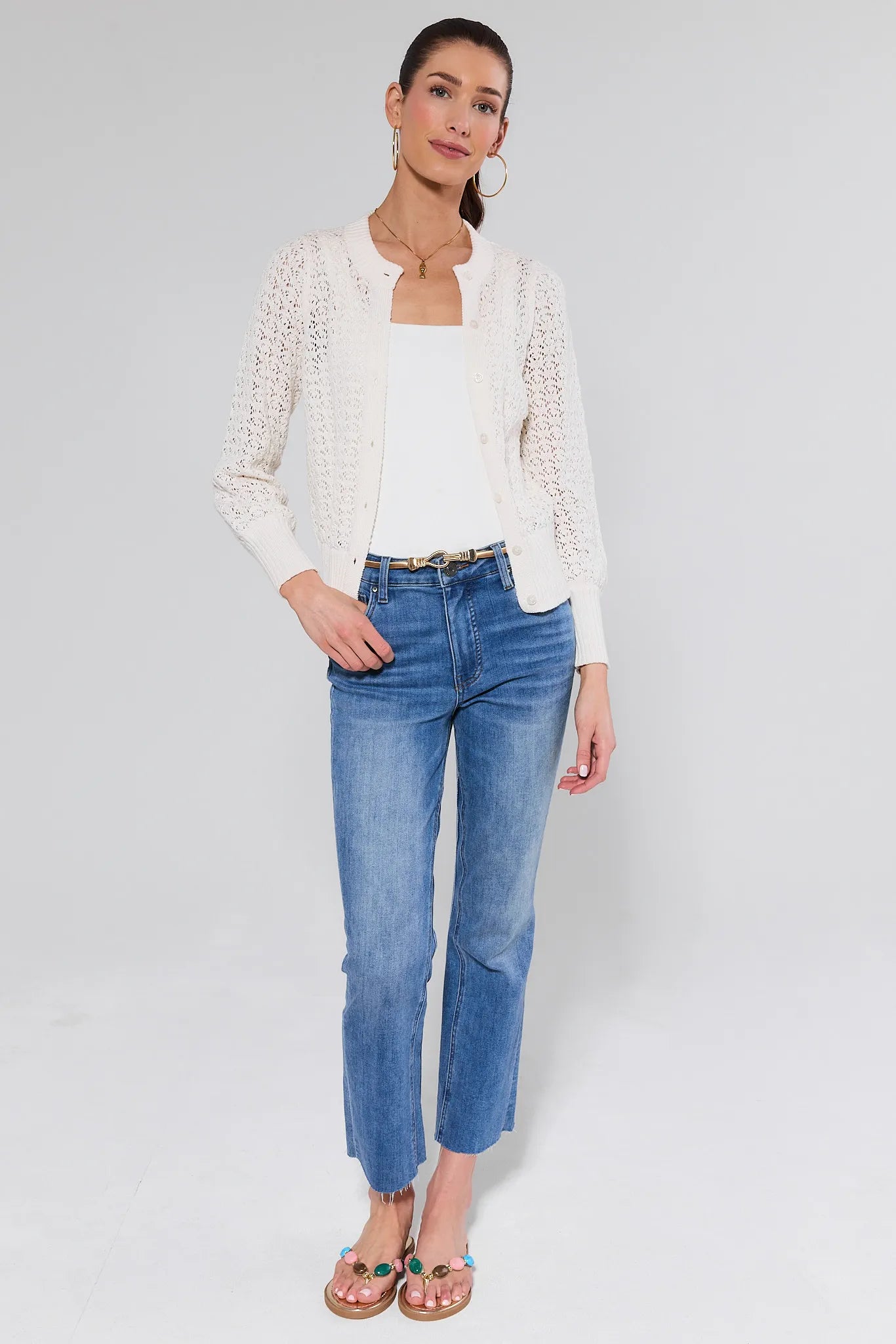 Woman wearing a white cardigan, white top, and blue jeans on a light gray background