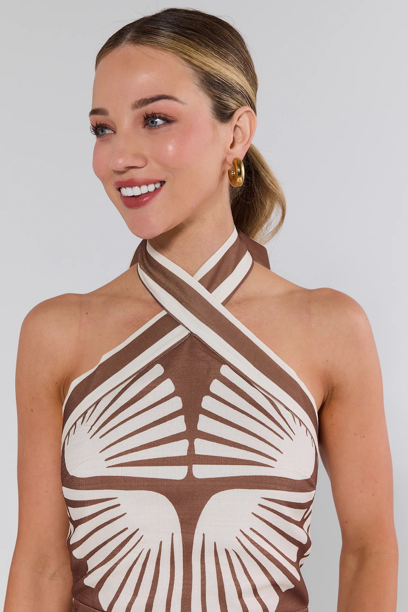 Woman wearing a brown and white patterned halter top against a plain background