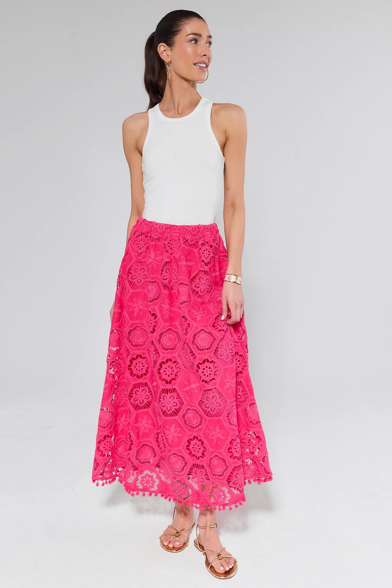 Woman wearing a white sleeveless top and pink lace skirt on a gray background